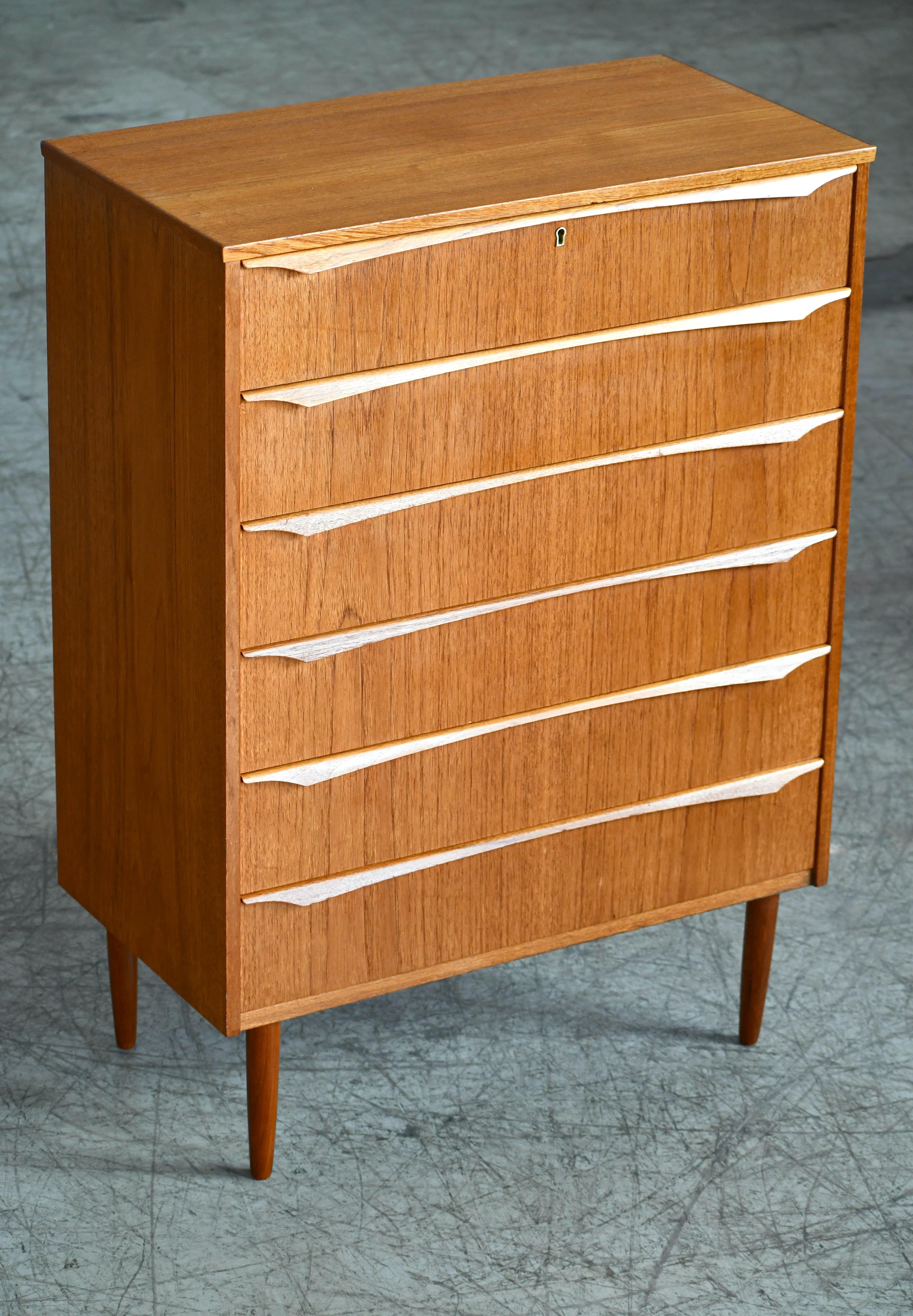 Beautiful Danish 1960s teak tall dresser or chest or drawers in the style of Kai Kristiansen. Sharp distinct design lines. Teak veneer with edges of solid teak and pulls carved from solid teak raised on solid tapered teak legs. Very nice color and