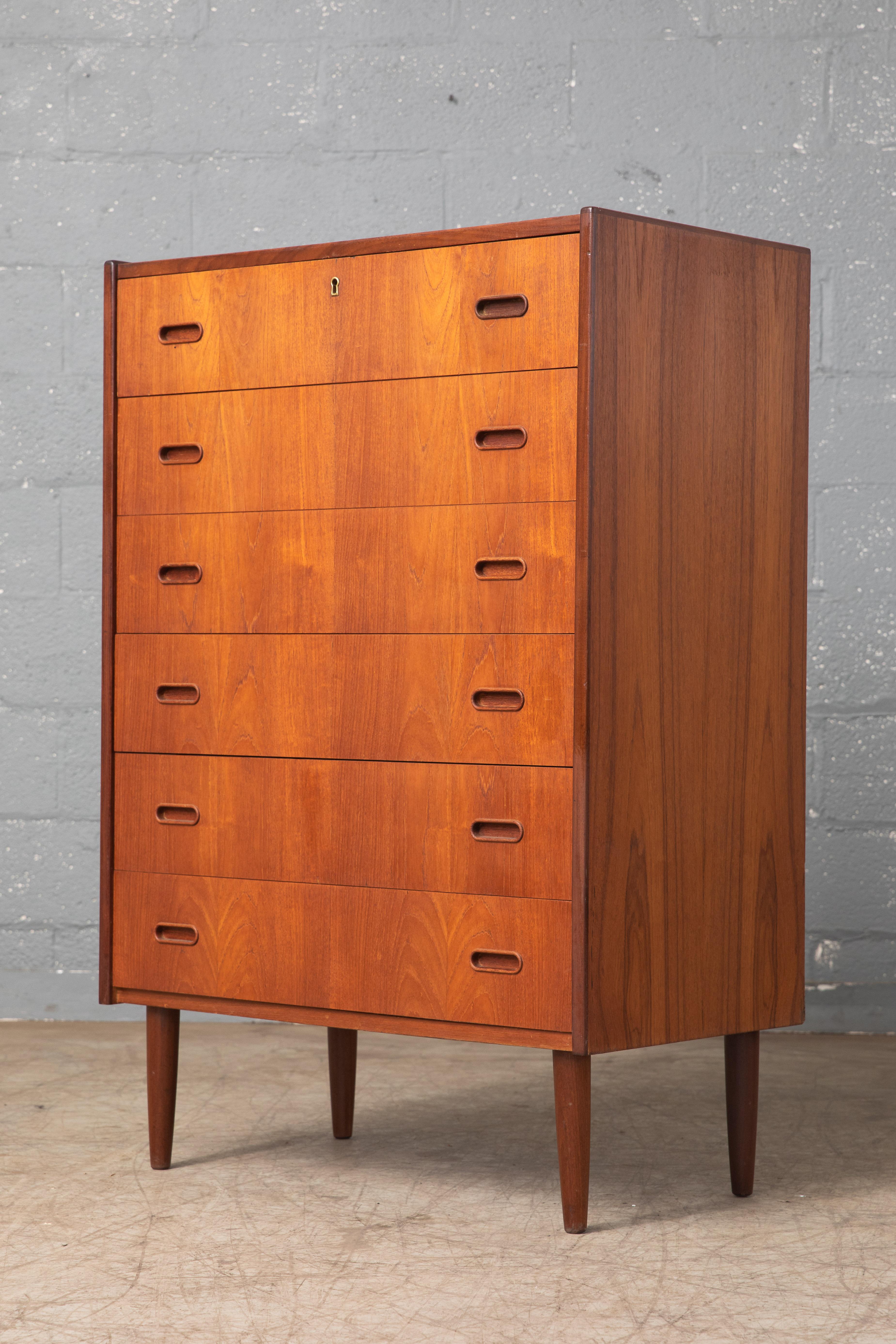 Beautiful Danish 1960s teak tall dresser or chest or drawers in the style of Kai Kristiansen. Sharp distinct design lines. Teak veneer with edges of solid teak and pulls carved from solid teak raised on solid tapered teak legs. Very nice color and
