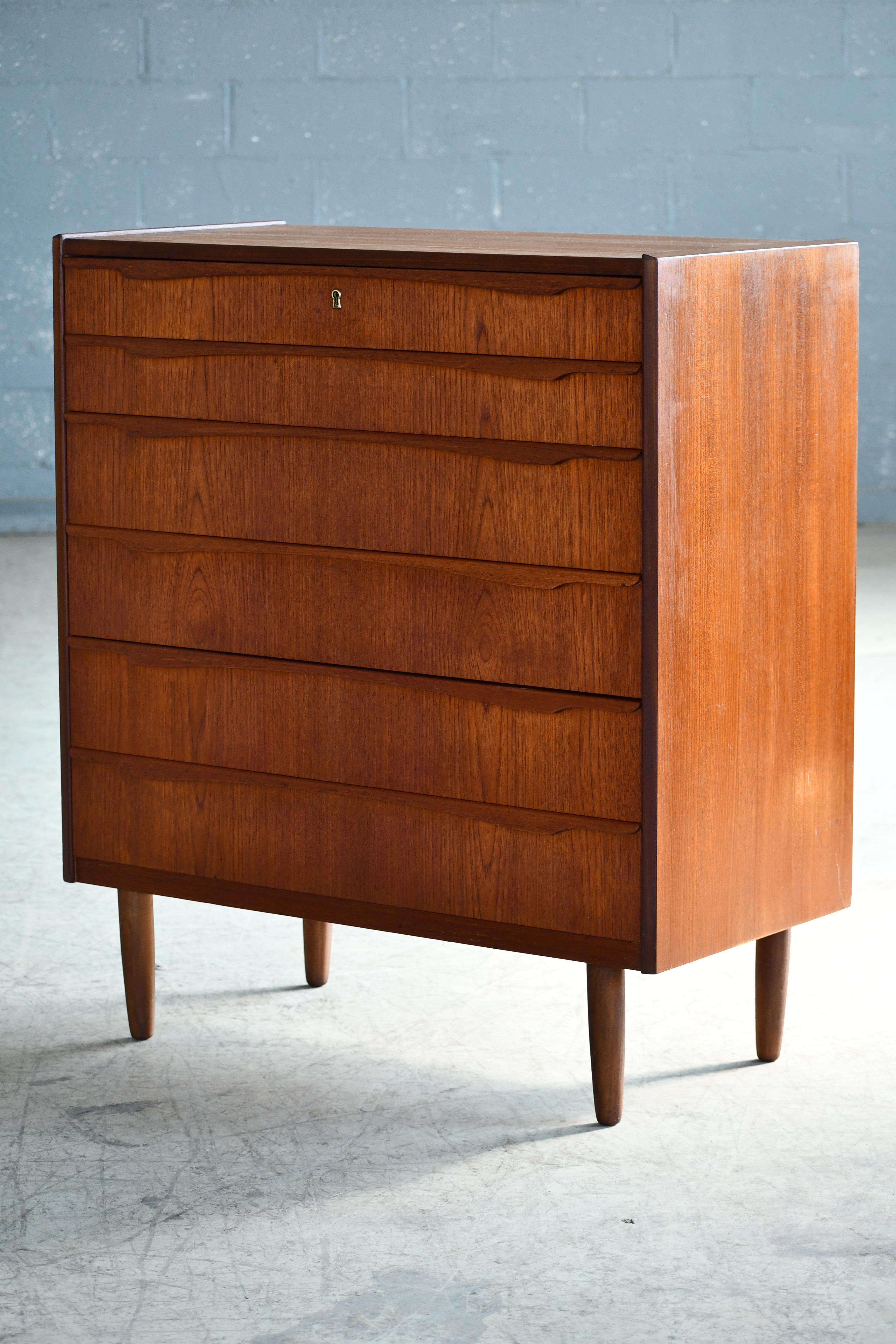 Beautiful Danish 1960s teak tall dresser or chest or drawers in the style of Kai Kristiansen. Sharp distinct design lines. Teak veneer with edges of solid teak and pulls carved from solid teak raised on solid tapered teak legs. Very nice color and