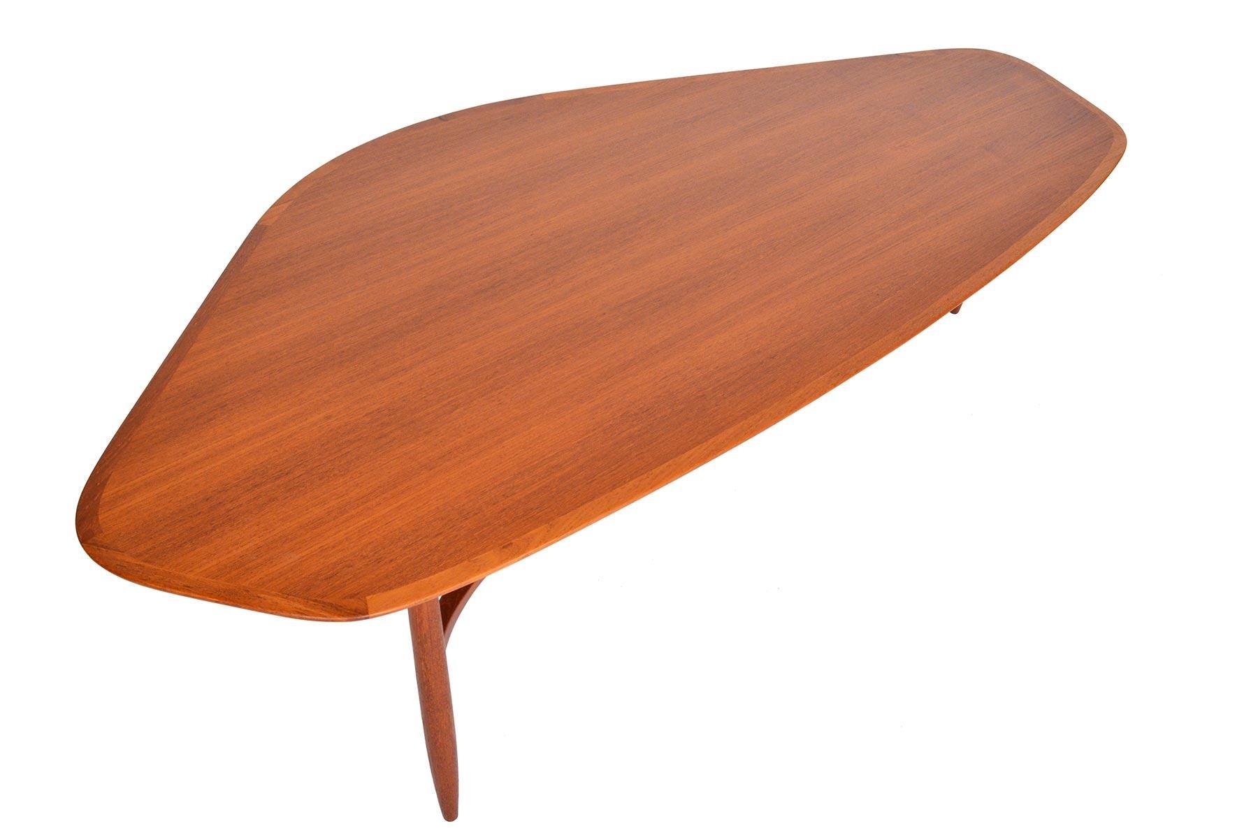 Sweeping angles and a long low design characterize this stunning Danish modern teak coffee table. Featuring a unique shape, this table is banded in a sleek teak frame. A beautiful three leg base is supported with sculpted braces. Recently refinished