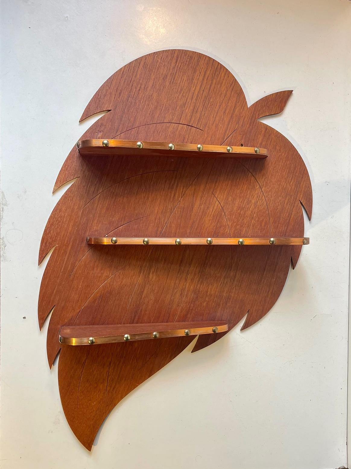 Skillfully crafted wall mounted spice-rack or display-shelf for small items in shape of a giant leaf. The 3 shelves features decor in copper-band set with brass nails. The shelver and back plate is made from teak veneer. Crafted by anonymous