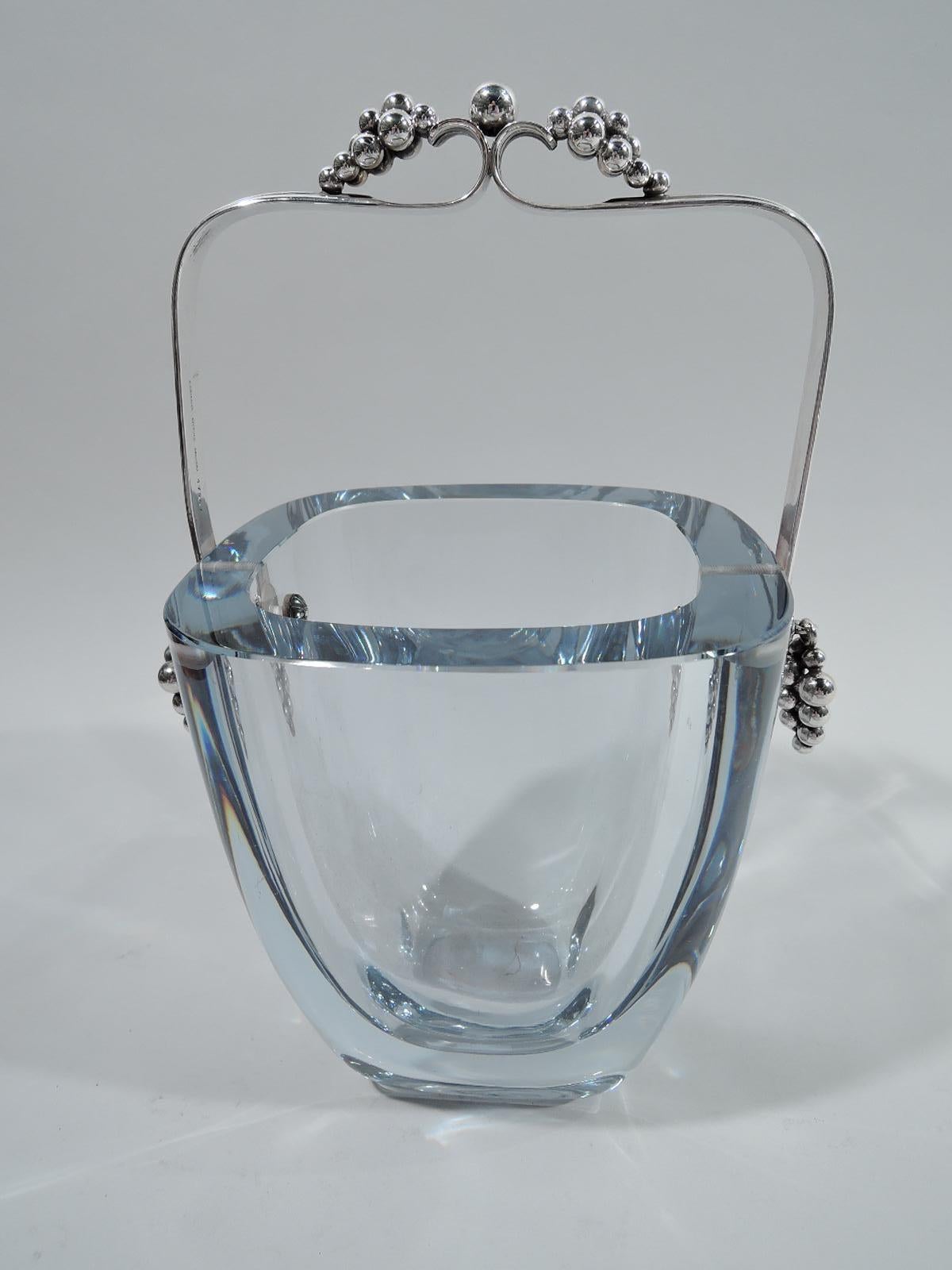 Mid-Century Modern ice bucket. Tapering sides, flat rim, and curved corners. Well ovoid. A thick, substantial vessel with swing-mounted sterling silver handle comprising 2 ribbed brackets with central dos-a-dos scrolls and grape bunch terminals