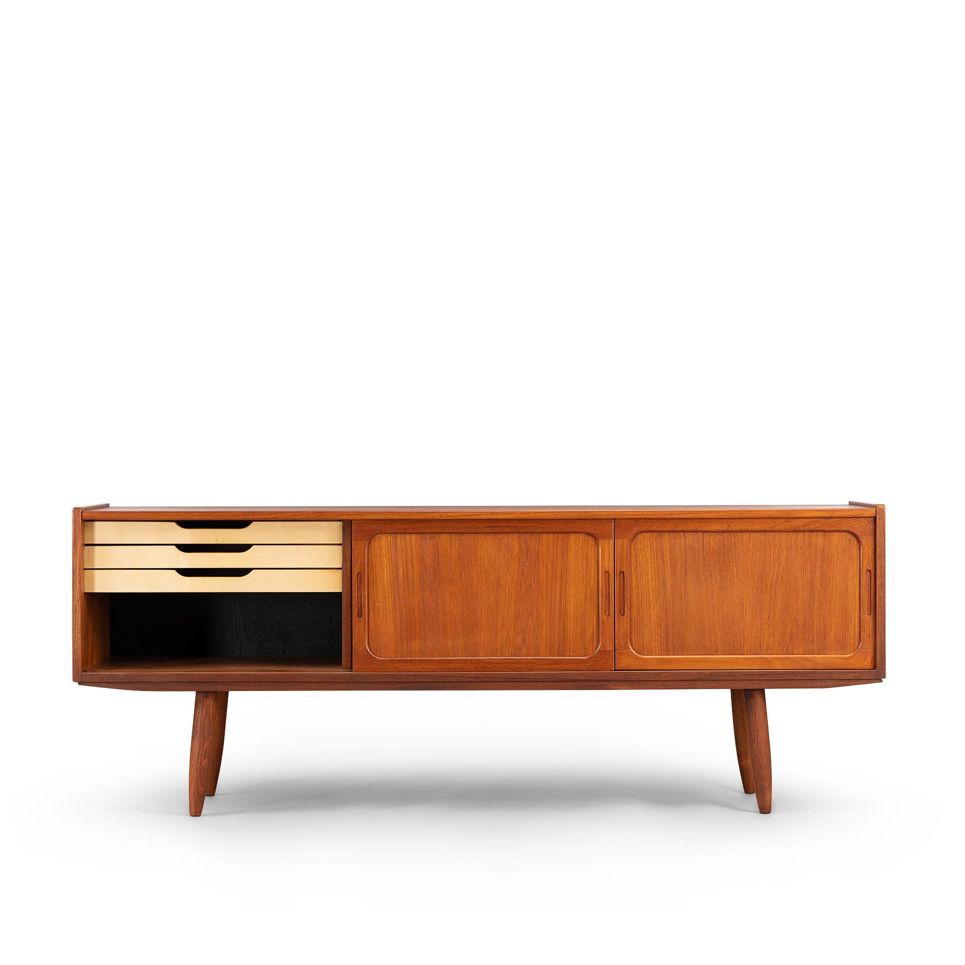 Low sideboard in teak in which you can hide all your pleasures. The color is a beautiful reddish dark brown. The cool grips, framed sliding doors and patterning of the wood make this one a true eyecatcher. On the inside there is all you need with a