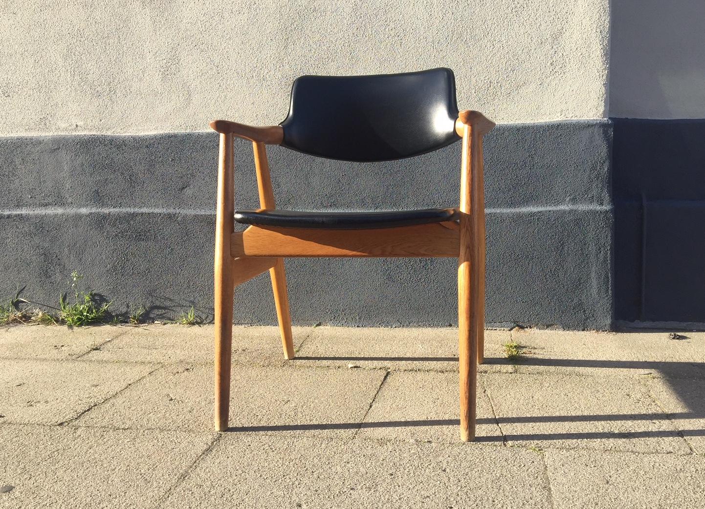 This Danish midcentury side chair with armrests was designed in 1952 by Erik Kirkegaard and manufactured in Denmark by Høng Stolefabrik in the 1960s. It features a frame in solid oak and the original black leatherette upholstery.