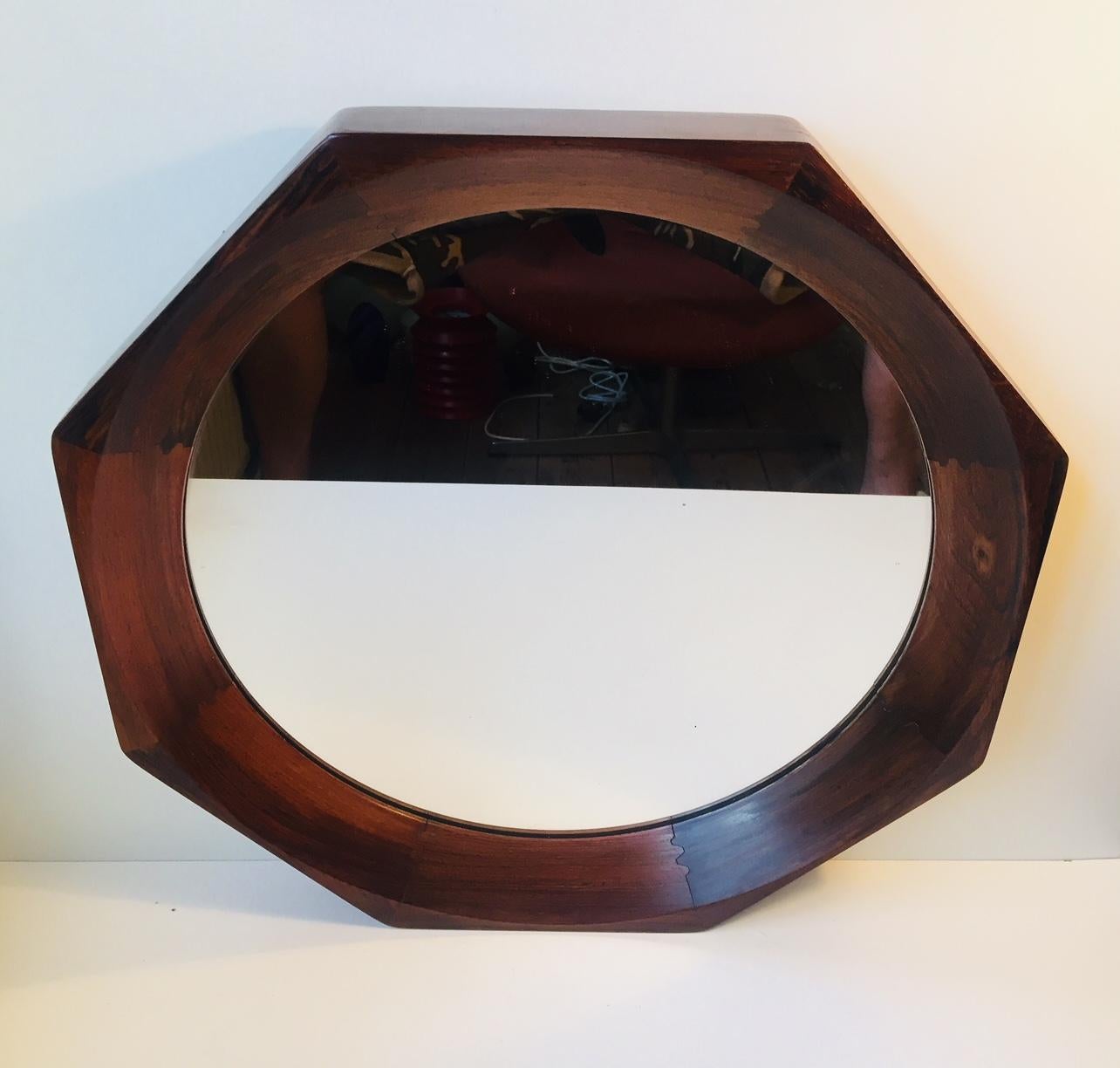This wall hung mirror was manufactured and designed by BVK in Denmark during the 1960s. BVK is best known for making small furniture for Illums Bolighus in Copenhagen. It features a solid and concave teak frame, round mirrored glass, secure wall