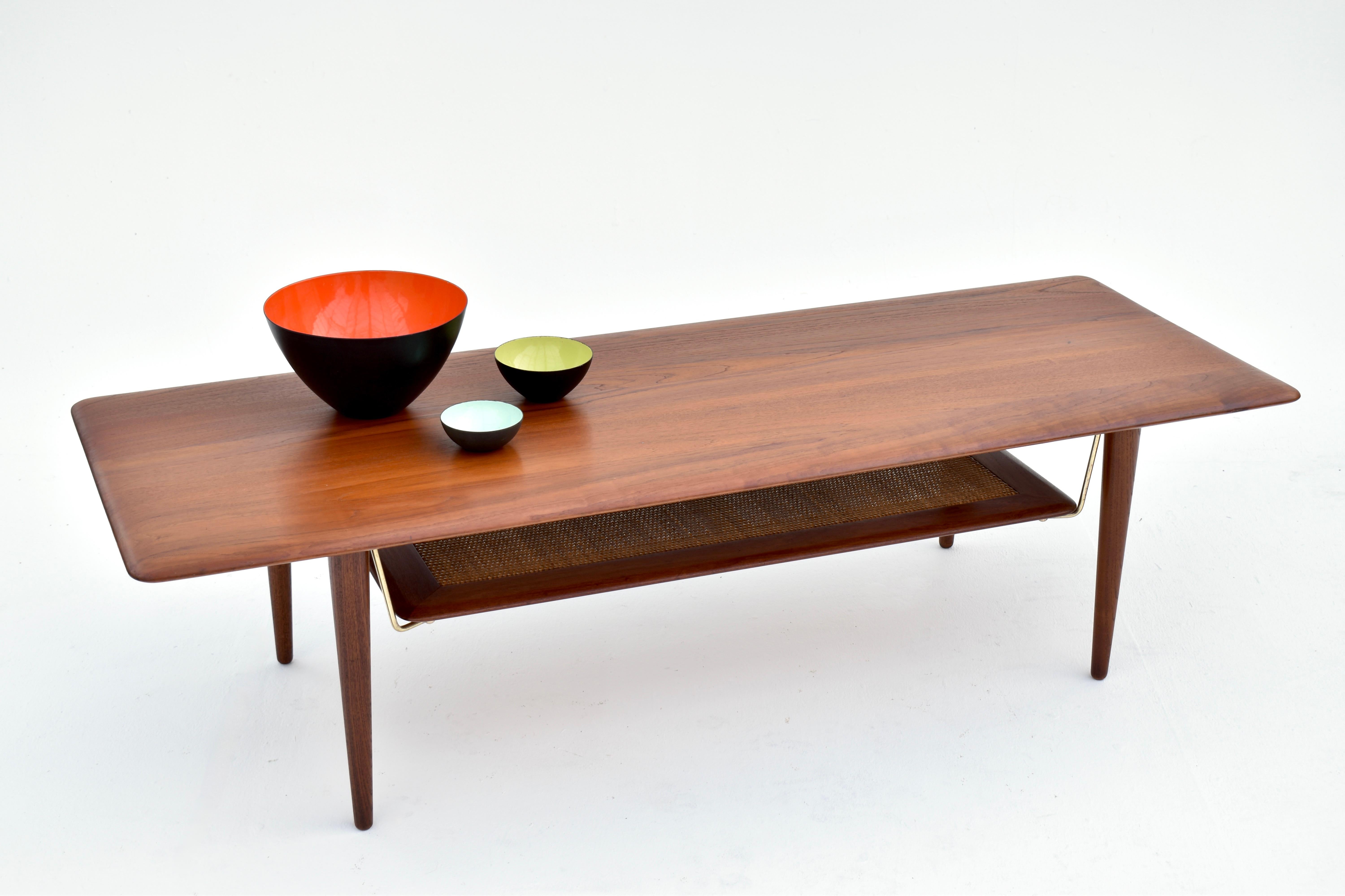Table basse longue construite en teck massif avec des accoudoirs en laiton subtil et un plateau inférieur en rotin. L'une des plus belles tables basses danoises du milieu du siècle, c'est un objet d'une beauté exquise conçu par deux des architectes
