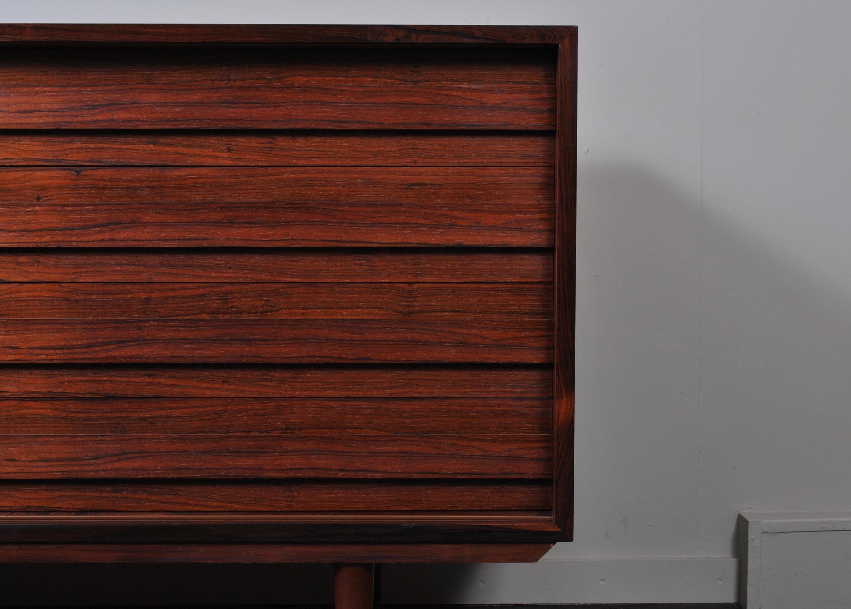 A modernist Danish midcentury rosewood sideboard by Dammand Rasmussen. Produced in Denmark circa 1960. Lovely color and in great condition. One sliding door to the left with an internal adjustable shelf and drawers to the right.