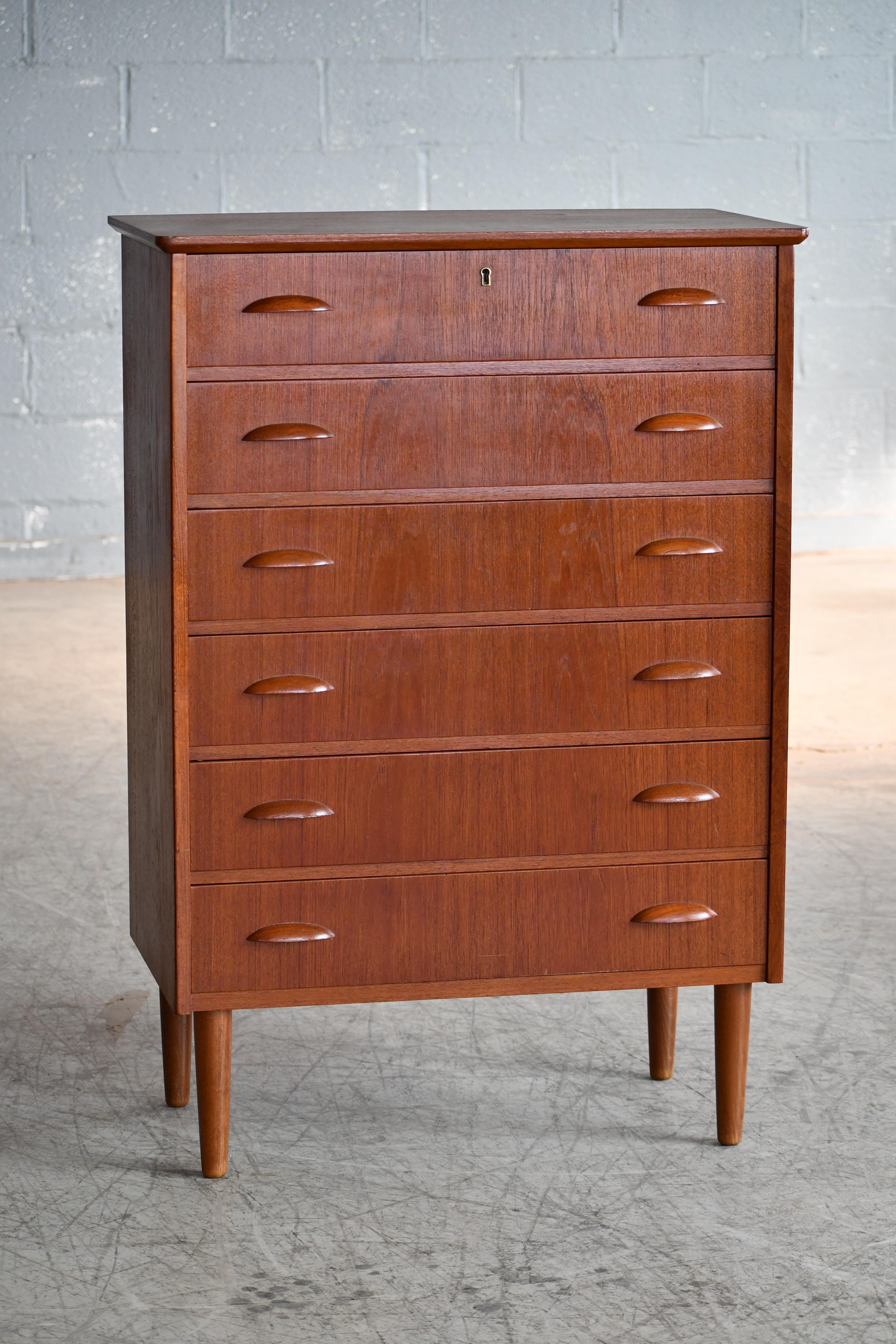 Beautiful Danish 1950s teak tall dresser or chest or drawers in the style of Kai Kristiansen. Sharp distinct design lines. Teak veneer with edges of solid teak and pulls carved from solid teak raised on solid tapered teak legs. Very nice color and