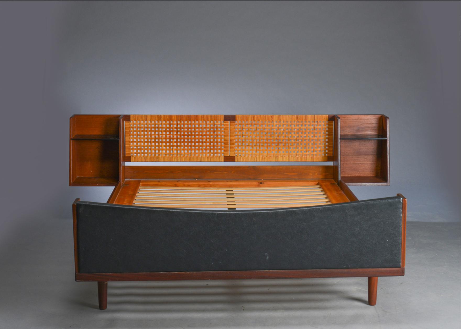 Elegantely shaped double bed model GE 701 designed by Hans Wegner in the 1960s and produced by Getama. The headboard is made of woven cane and has floating side tables with black glass removable shelves to each side of the bed. Teak structure and