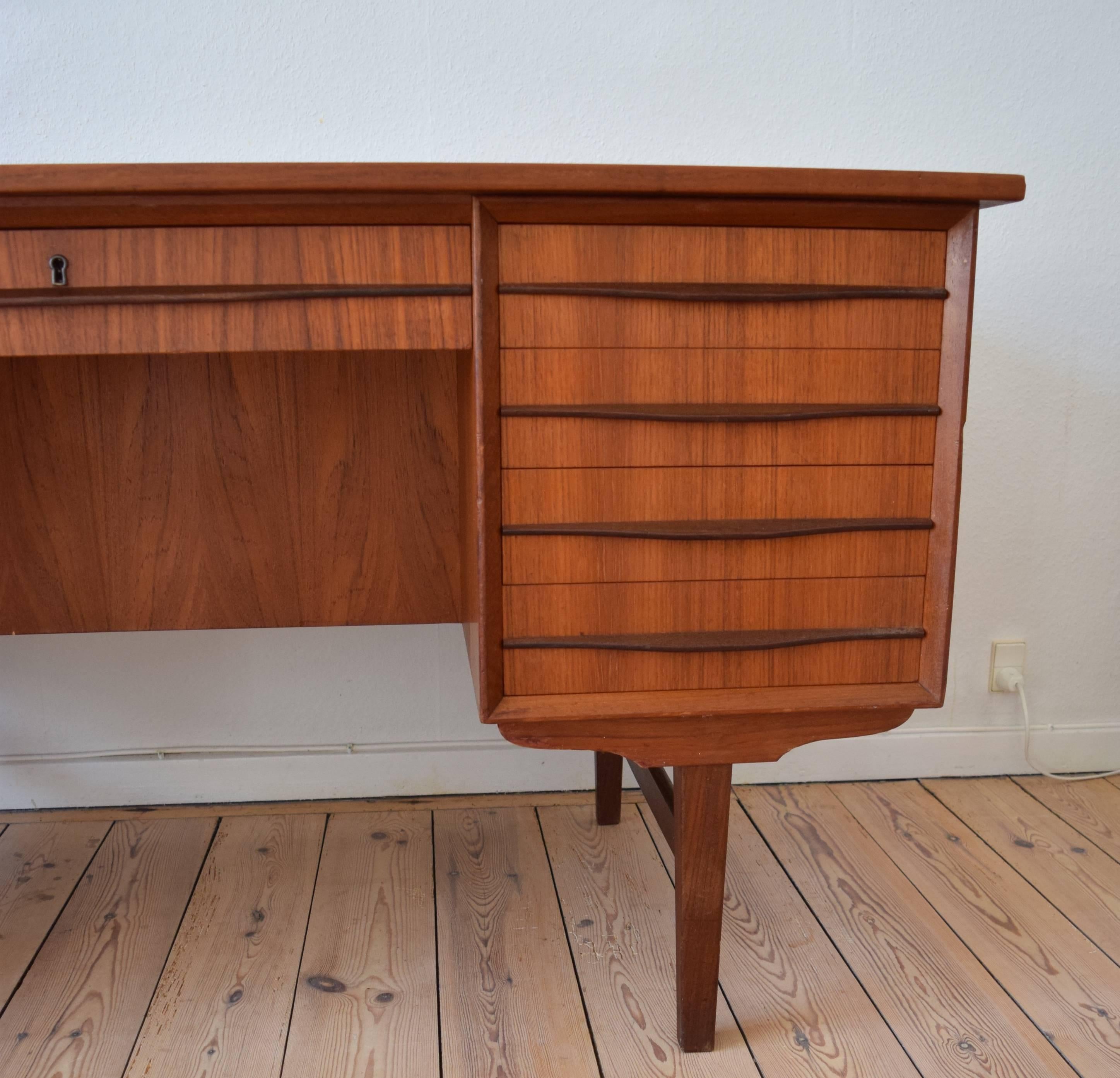 Teak executive desk manufactured in Denmark in the 1960s. Desk features seven drawers on the front, and bar cabinet and bookshelves on the back side. The full-length teak handles are unusual in that they sit on the centre of the drawer. Sits on