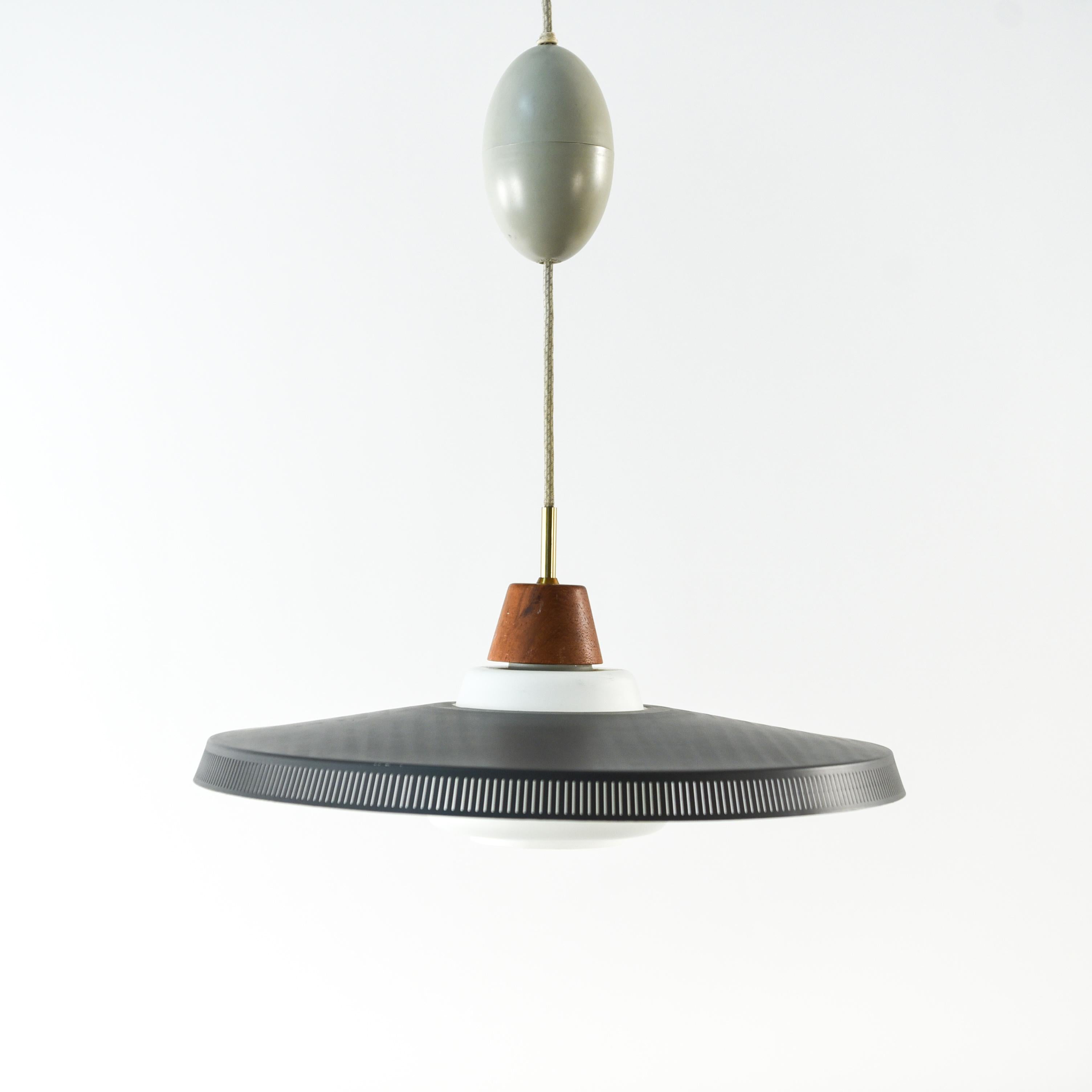 This Danish midcentury pendant light was designed by Bent Karlby for Lyfa, circa 1950s. It features a perforated metal shade with a teak accent above. This piece has an interesting, unusual shallow saucer form.