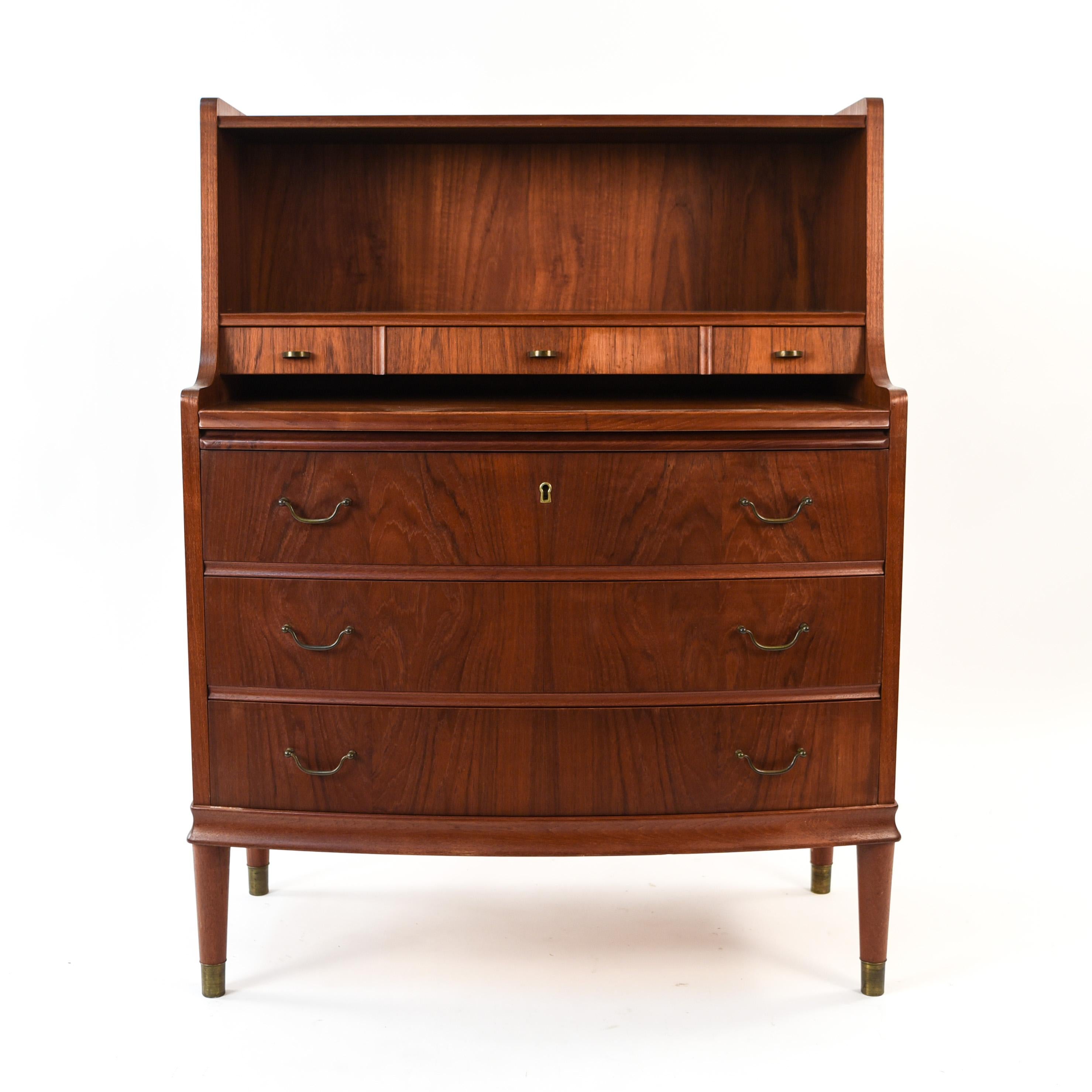 This Danish midcentury secretaire is made of teak wood, circa 1960s. This piece combines the traditional feel of the hardware and curved front with the Scandinavian Modern silhouette, making it a versatile piece that would fit right into virtually