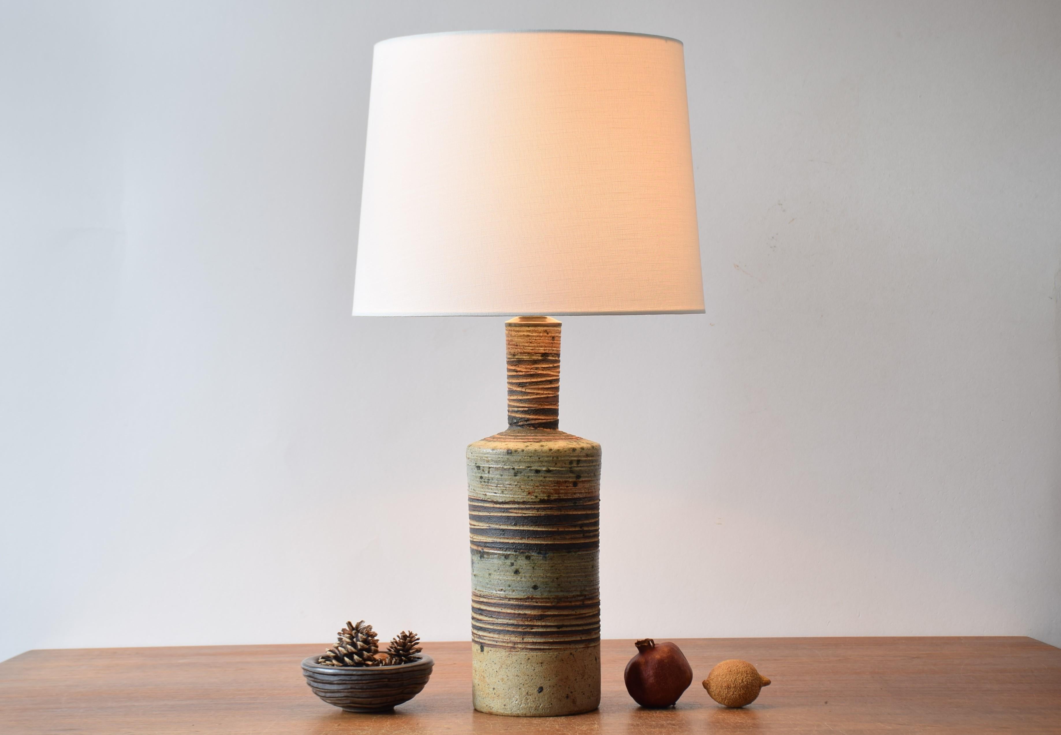 Tall table lamp including lamp shade by Danish ceramist Tue Poulsen (born 1939). Made ca. 1970s in Tue Poulsen´s own studio.
The base is made of chamotte clay and has incised stripes. It partly shows the warm beige clay and partly it´s decorated