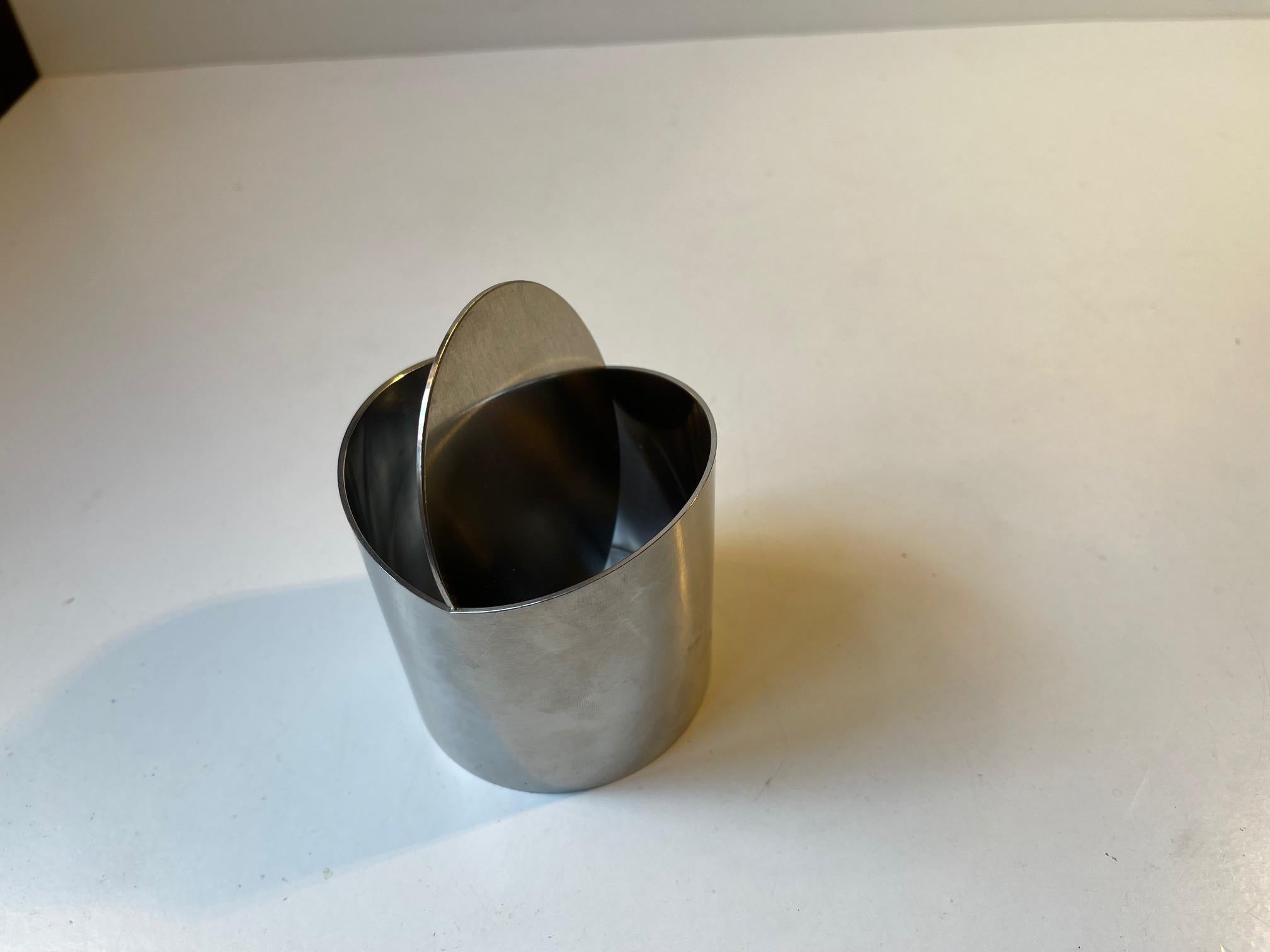 A stylish stainless steel ashtray designed by Roelandt and manufactured by Stelton in Denmark during the 1980s. Similar to Arne Jacobsen's cylinda-line but with a tilting mechanism/lid instead. Imprinted with designer and makers marks beneath the