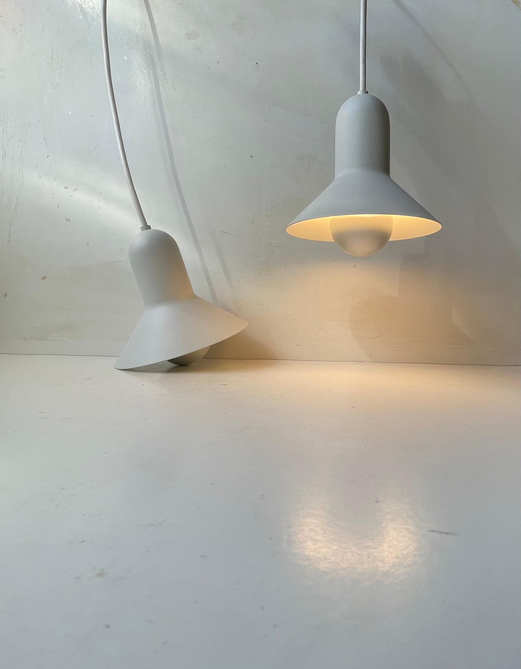 Un par de pequeñas lámparas colgantes blancas de metal blanco. Estricta apariencia minimalista combinada con curvas orgánicas. Este modelo se llama Confetti y fue diseñado por el arquitecto danés Claus Bonderup y fabricado por Focus en Dinamarca a