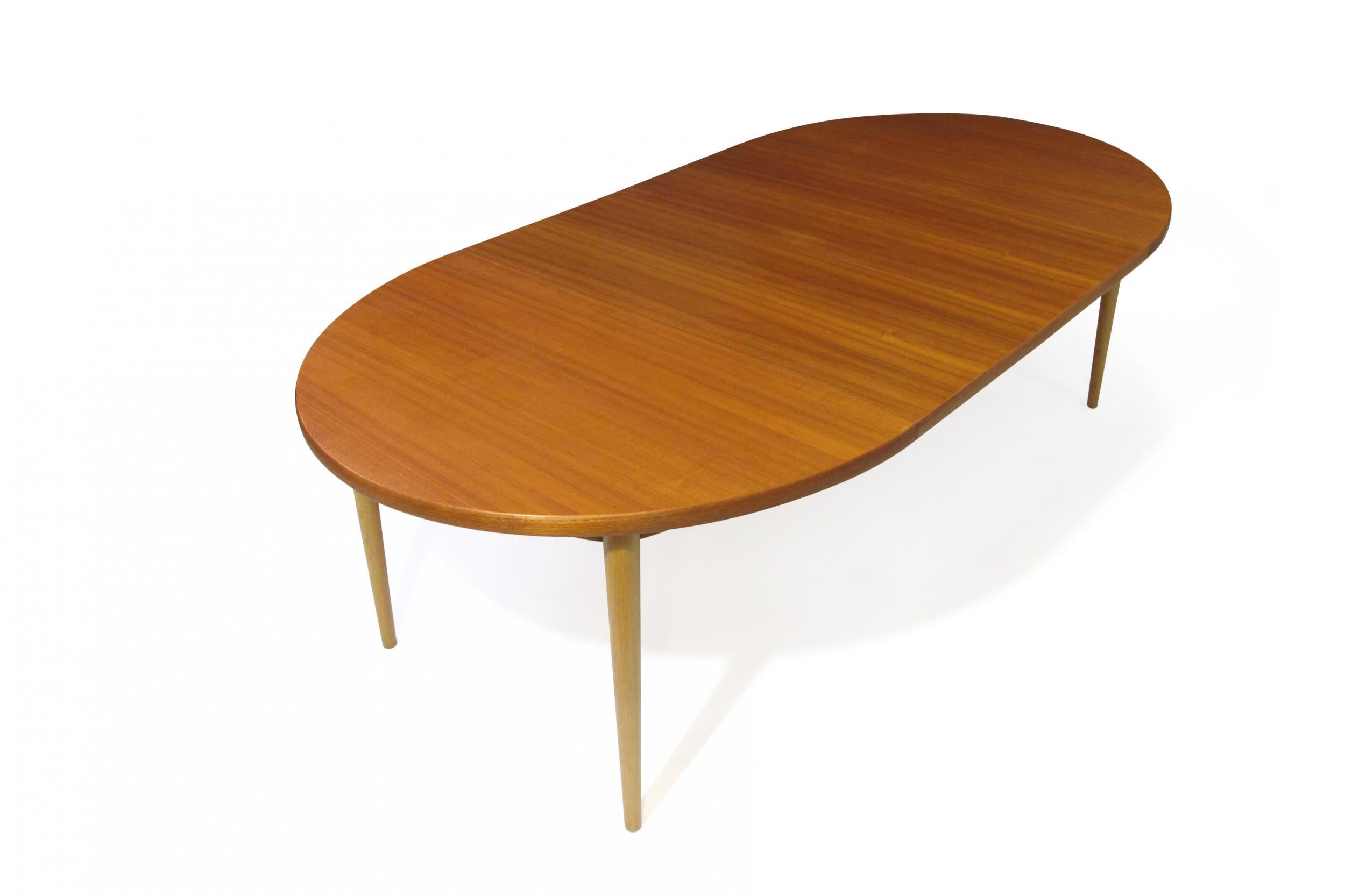 MM Moreddi oval teak dining table with two insert leaves raised on solid oak tapered legs. Table for 6, 8, or 10 guests. The table has an MM Moreddi stamp under the table. Measures: 55