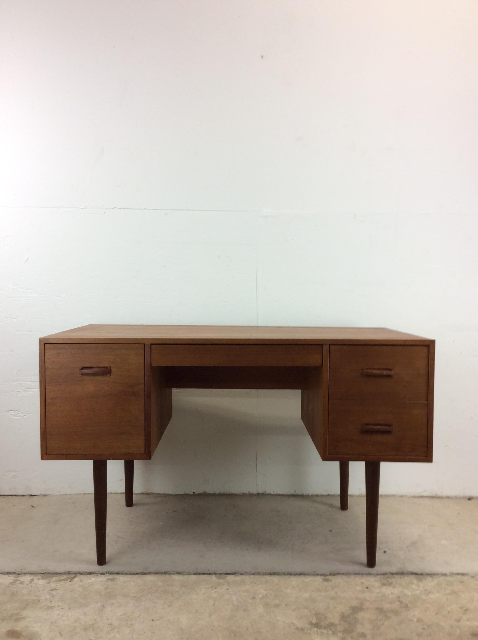 This Danish modern writing desk features pressed wood construction, original teak veneer, four dovetailed drawers with carved wood pulls, finished back and tall tapered legs. 

Please see our listings for complimentary Danish Modern pieces.