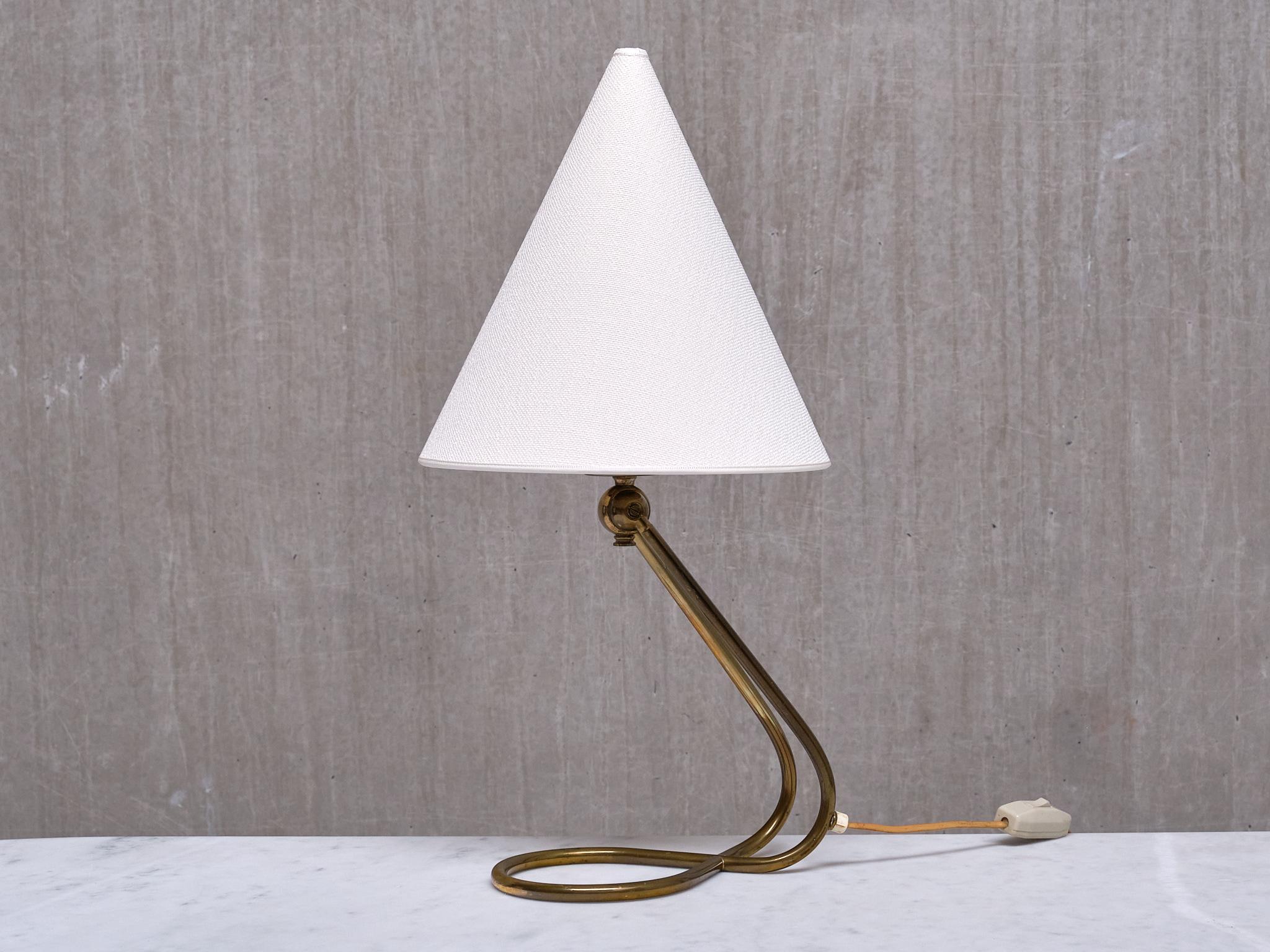 This rare table or desk lamp was produced in Denmark in the 1950s.

The lamp features a continuous tubular brass loop, which seamlessly forms both the base and the arm in one elegant piece, giving the lamp an airy, almost floating quality. The