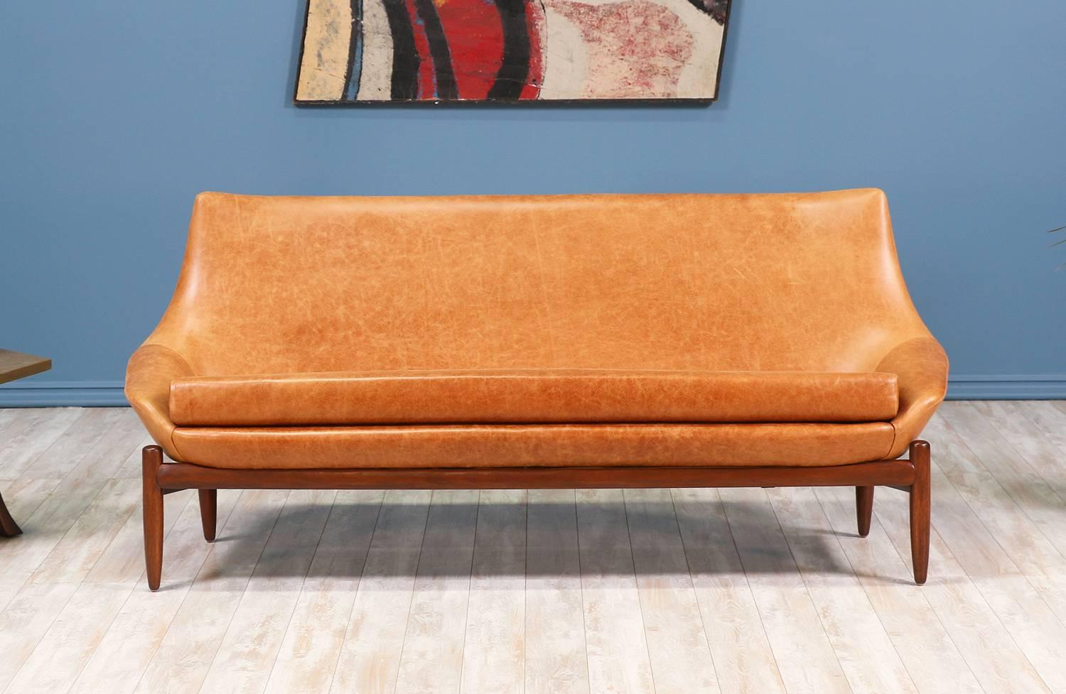 Mid-Century modern sofa designed and manufactured by Danish De Luxe in Australia circa 1960’s. This unique sofa features a solid walnut wood sculptural base with a comfortable seat that has been reupholstered in an elegant full-grain cognac leather.
