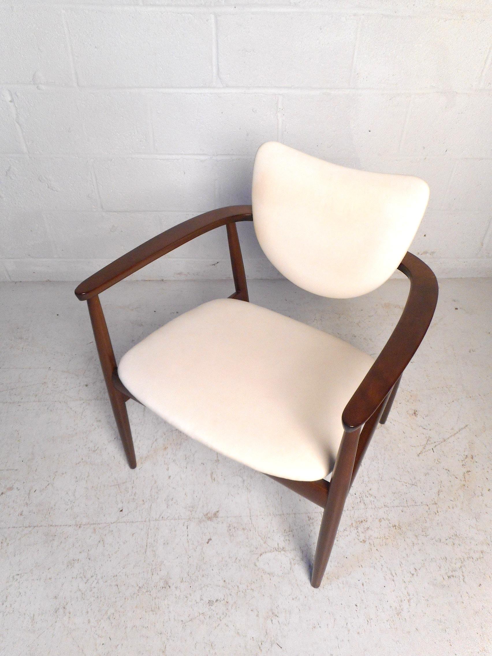 This impressive Danish modern chair features a sturdy finished walnut frame, sleek white faux-leather upholstery, sculpted armrests, and an interestingly contoured backrest giving the chair a unique visual profile. This chair is sure to compliment