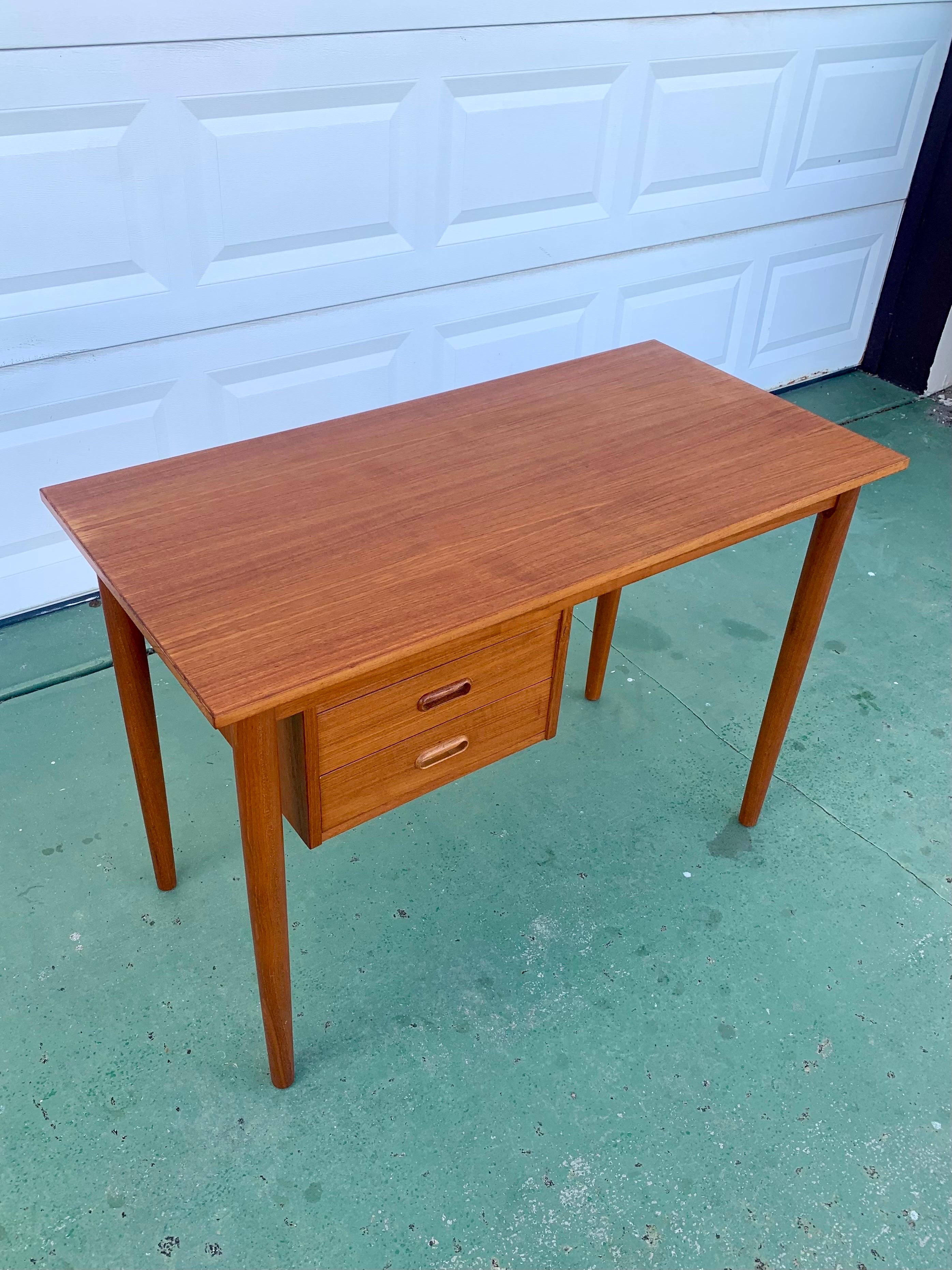 Mid-Century Modern writing desk in teak. Made in Denmark. Beautiful solid teak legs and skirt. With a beautifully veneered top with a border. The top has been refinished and the piece is in excellent condition. 

Two drawers for storage and it’s