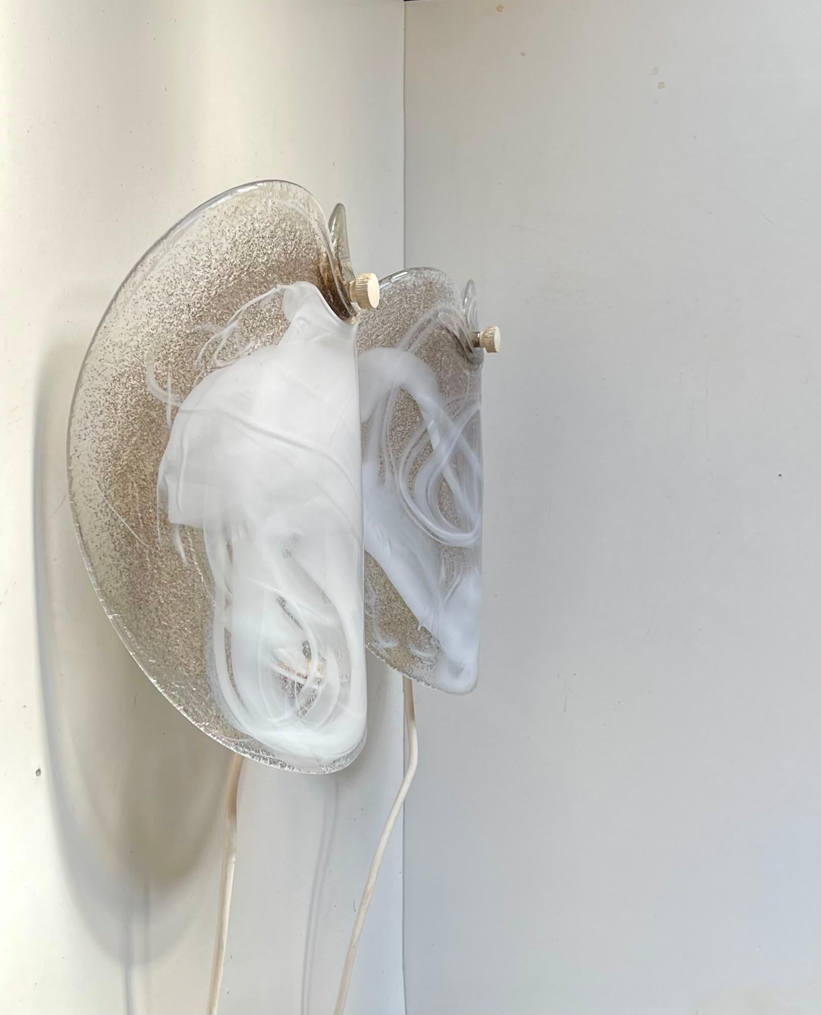 Apliques circulares curvos hechos de grueso vidrio soplado a mano con polvo de bronce y cobre incrustado y remolinos abstractos de vidrio blanco que hacen las veces de difusores/suavizadores de luz. Este modelo se llama Glasplattelampet (lámpara de