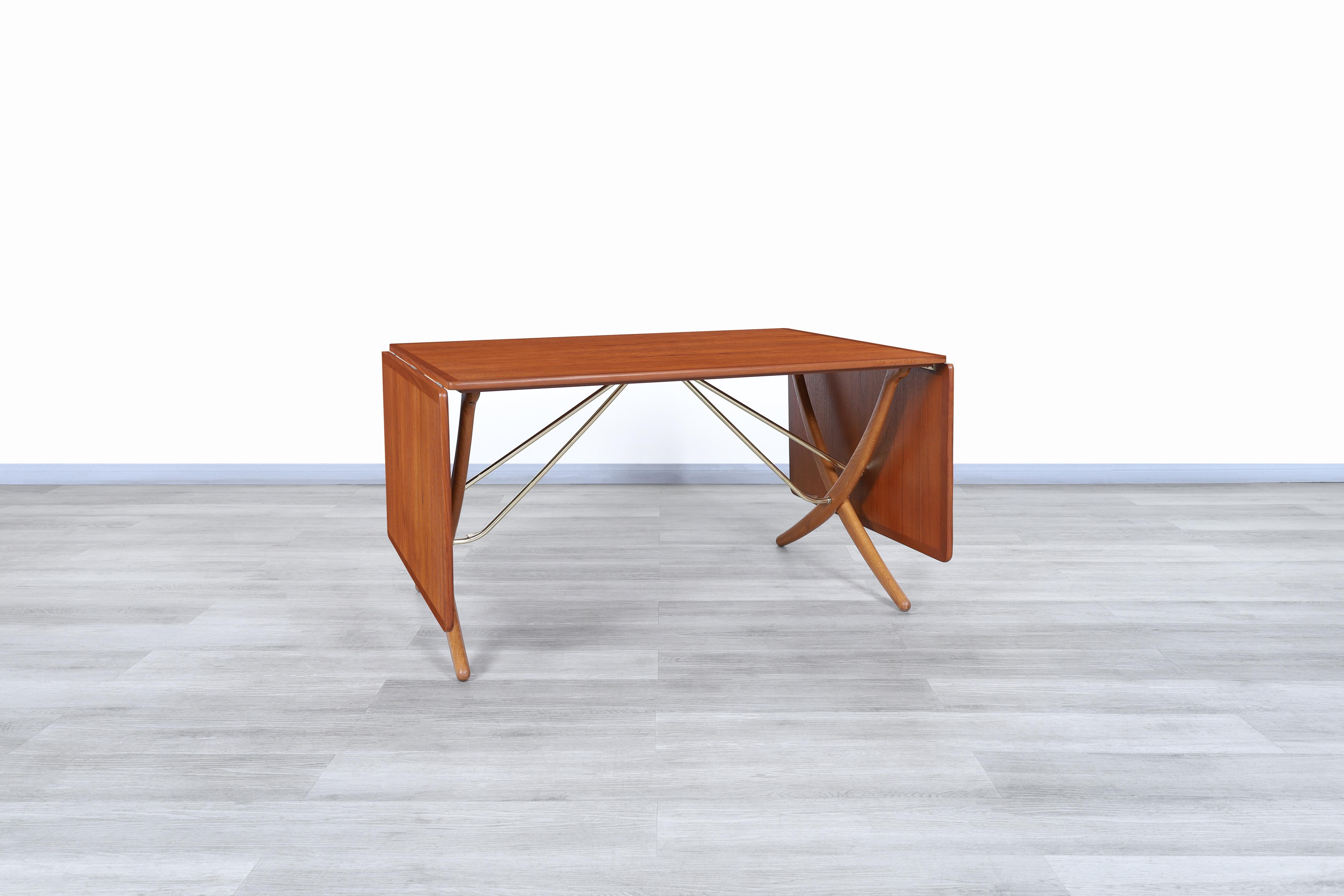 Exceptionnelle table de salle à manger danoise à pieds de sabre, conçue par Hans J. Wegner pour Andreas Tuck au Danemark en 1955. Cette table emblématique AT-304 est composée d'un plateau en teck et de deux feuilles tombantes. Les pieds sabres