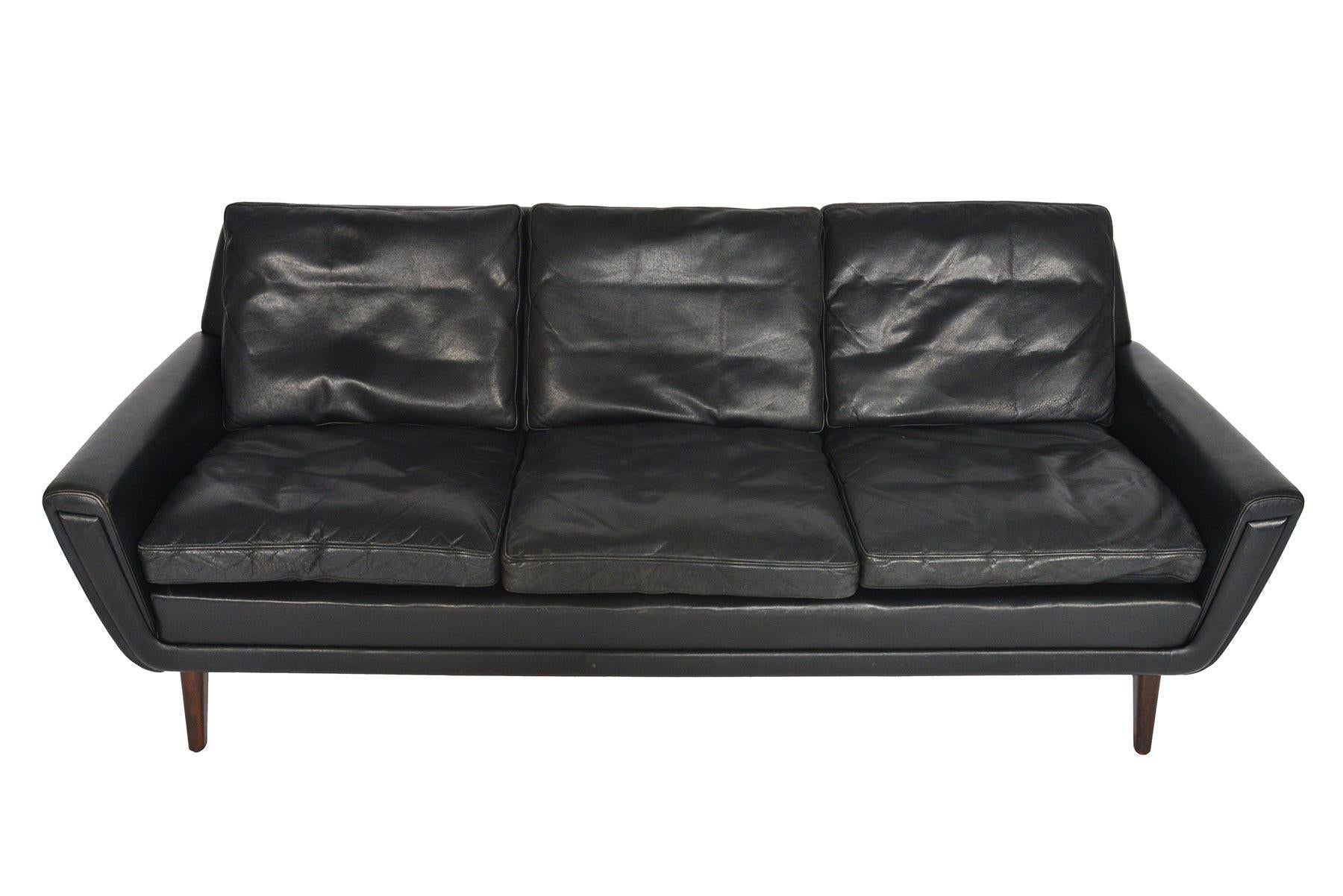 This Danish modern three-seat sofa in black leather hails from the 1960s and will blend perfectly with any modern decor. The gondola style frame features atomic armrests that organically flow from either side. Six down- filled leather cushions sit