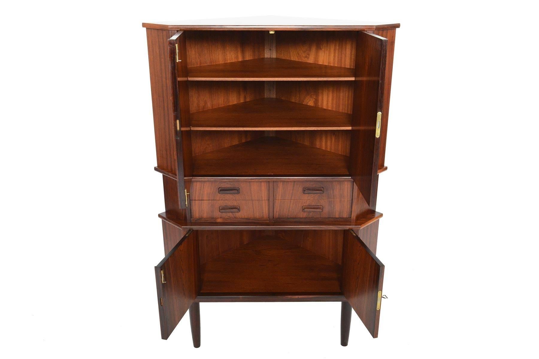 This Danish modern Brazilian rosewood corner cabinet is the perfect storage solution for any home. This piece offers two cabinet spaces and a bank of four drawers with atomic pulls nestled in the centre. Cabinets unlock to reveal open storage with