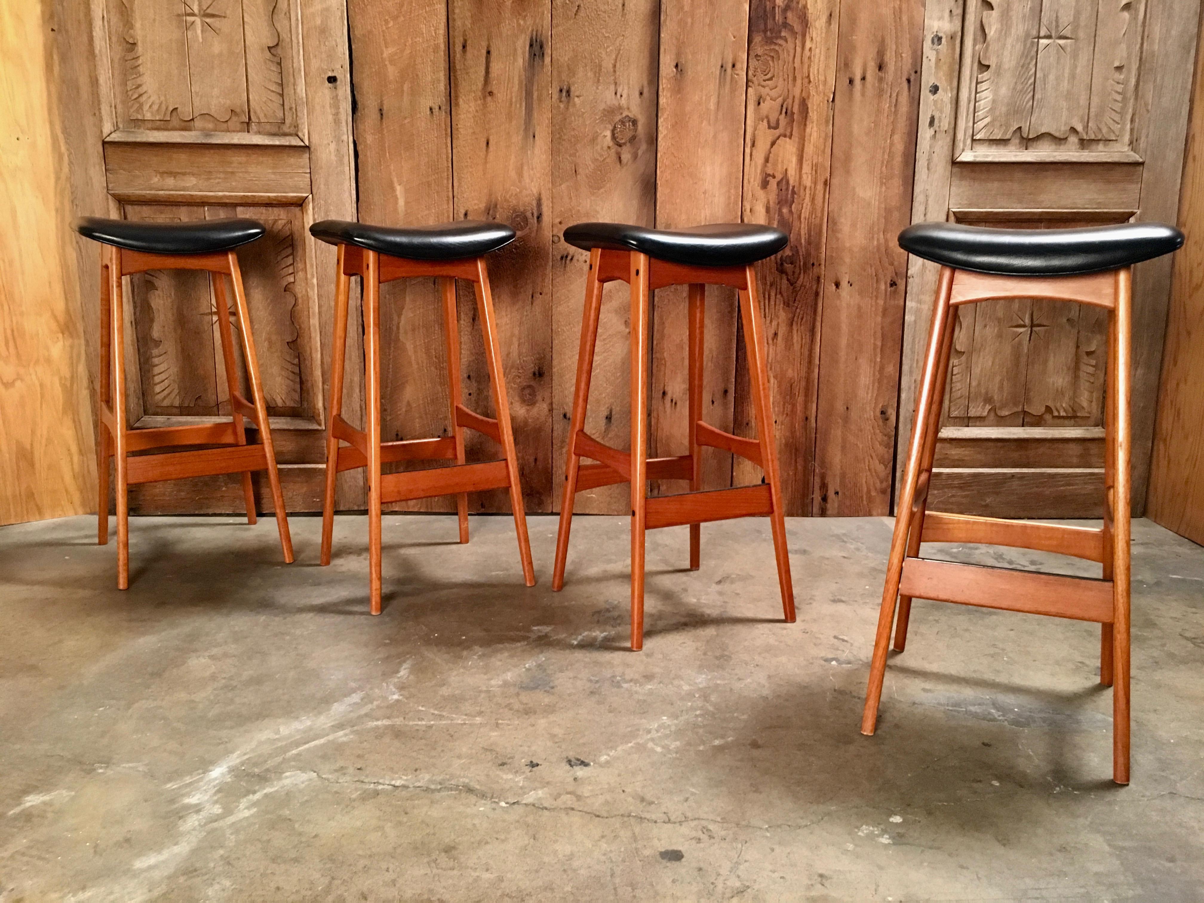 Set of four Mid-Century Modern teak stools with black metal protector on the footrest and black vinyl seats.