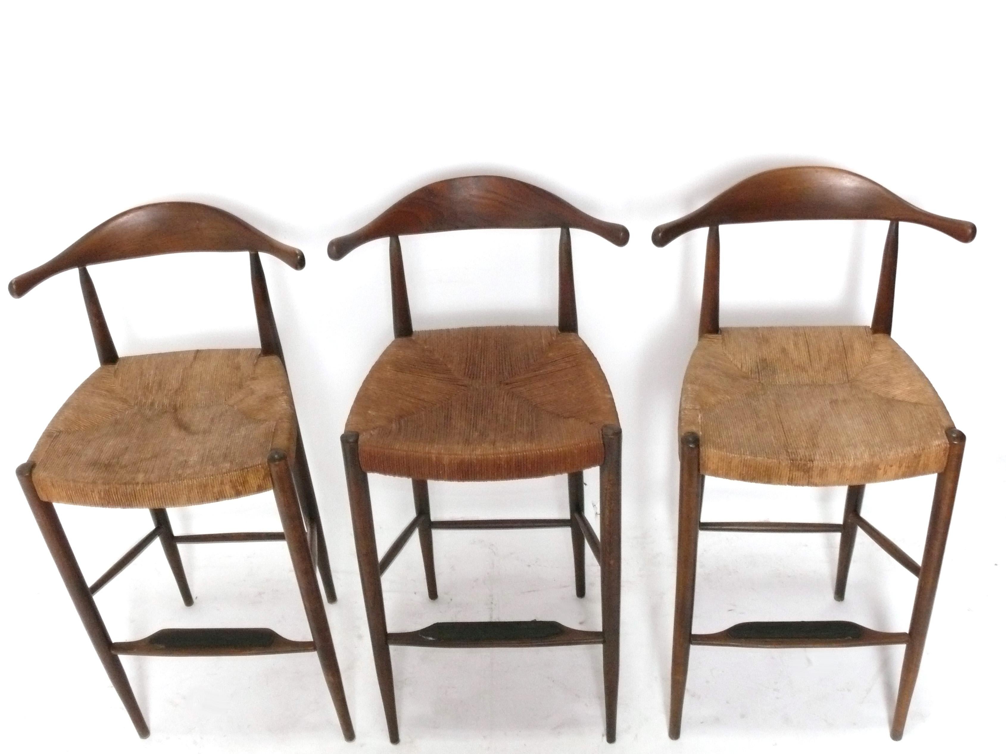Set di tre sgabelli da bar moderni danesi, Danimarca, anni '60 circa. Sono costruite con telai in teak e sedute in giunco intrecciato. Come si vede dalle foto, i sedili presentano alcune macchie d'acqua e un sedile è leggermente più scuro degli