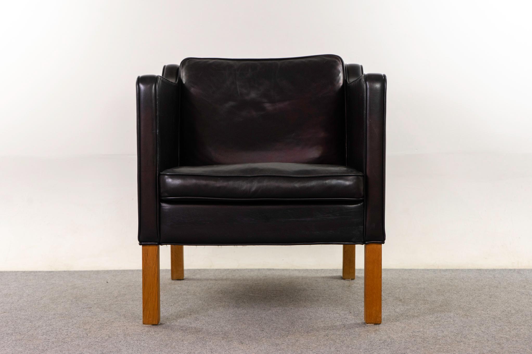 Leather Danish lounge chair, circa 1960s. Jet black leather and contrasting oak legs. Sleek modern lines, piped edging, loads of life in it yet! Original upholstery with minor wear. 

