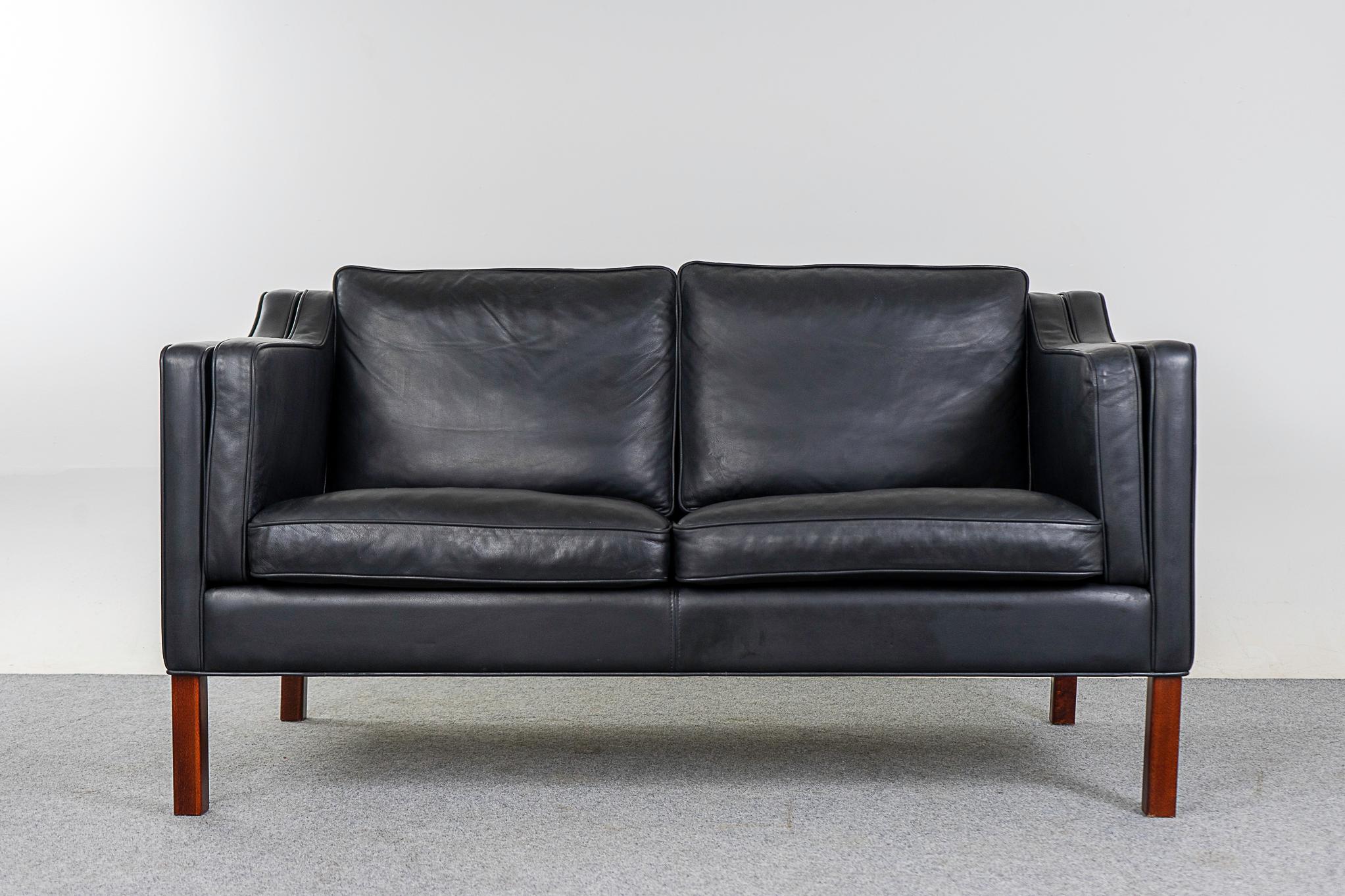 Leather mid-century loveseat, circa 1960's. Original pitch black leather in great condition! Solid wood legs and robust construction. Simple modern lines to suit any decor. Very comfortable, cozy up!