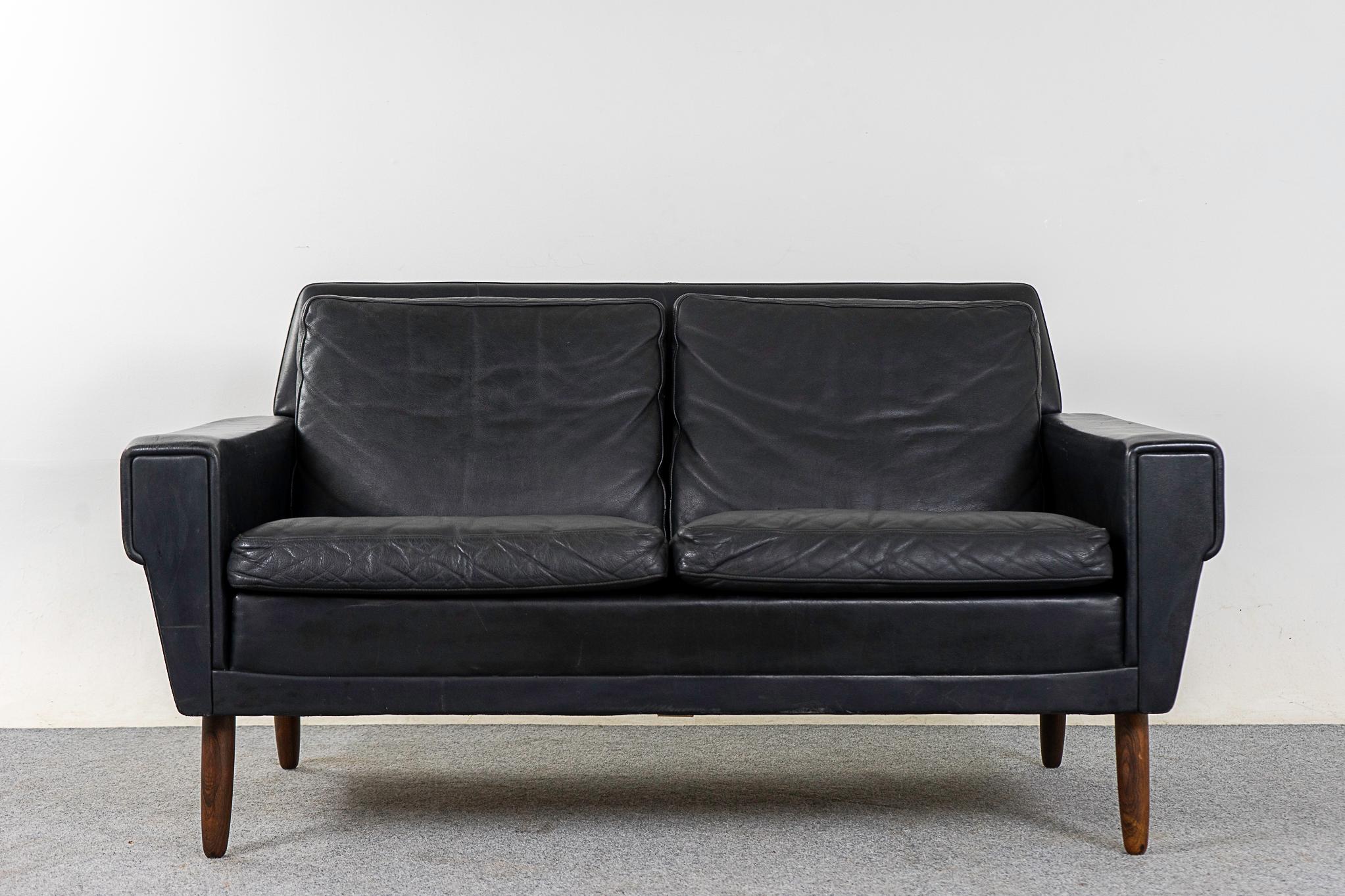 Leather and rosewood Danish loveseat, circa 1960's. Sultury andles on thi charming lover. Original black leather upholstery with nice patina. Solid splayed tapering rosewood legs.  Some wear and tear, as shown in photos.

Please inquire for remote