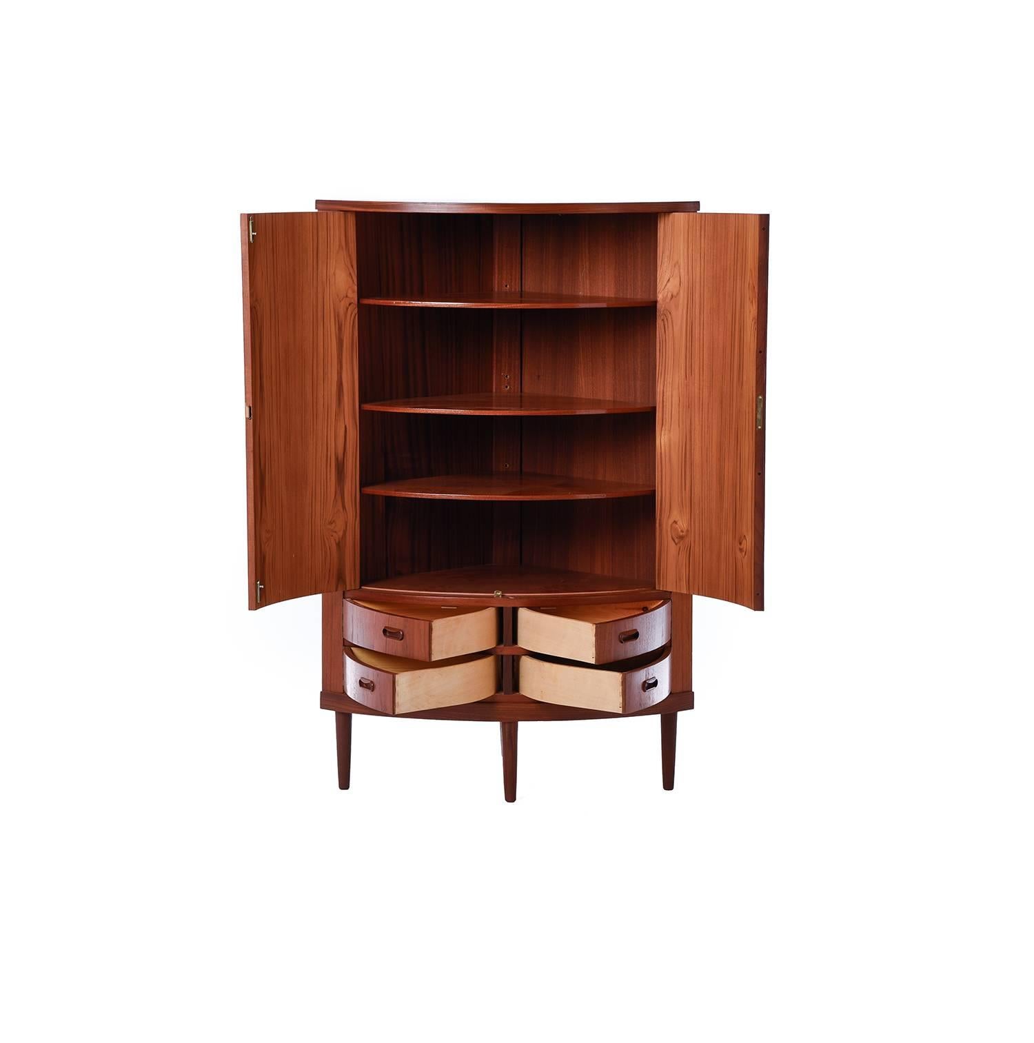 This unique bow front corner cabinet in teak provides extensive storage options with multiple swing-open drawers and adjustable interior shelves.