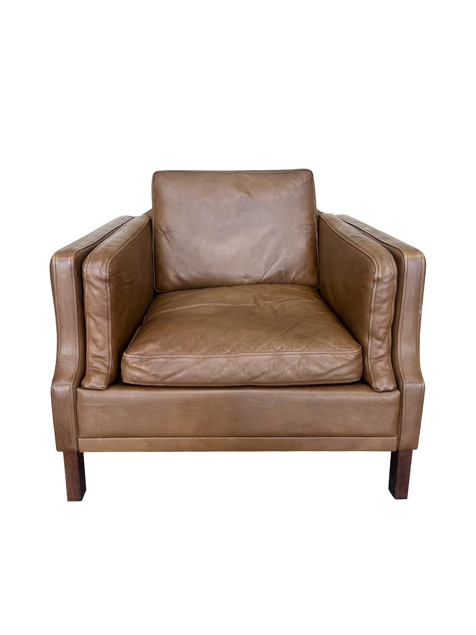 Fabricado en la década de 1970, este sillón de cuero marrón fue diseñado al estilo de Børge Mogensen. Al igual que las sillas de Mogensen, este sillón presenta líneas suaves que se curvan y suavizan en las esquinas. Los amplios asientos abiertos