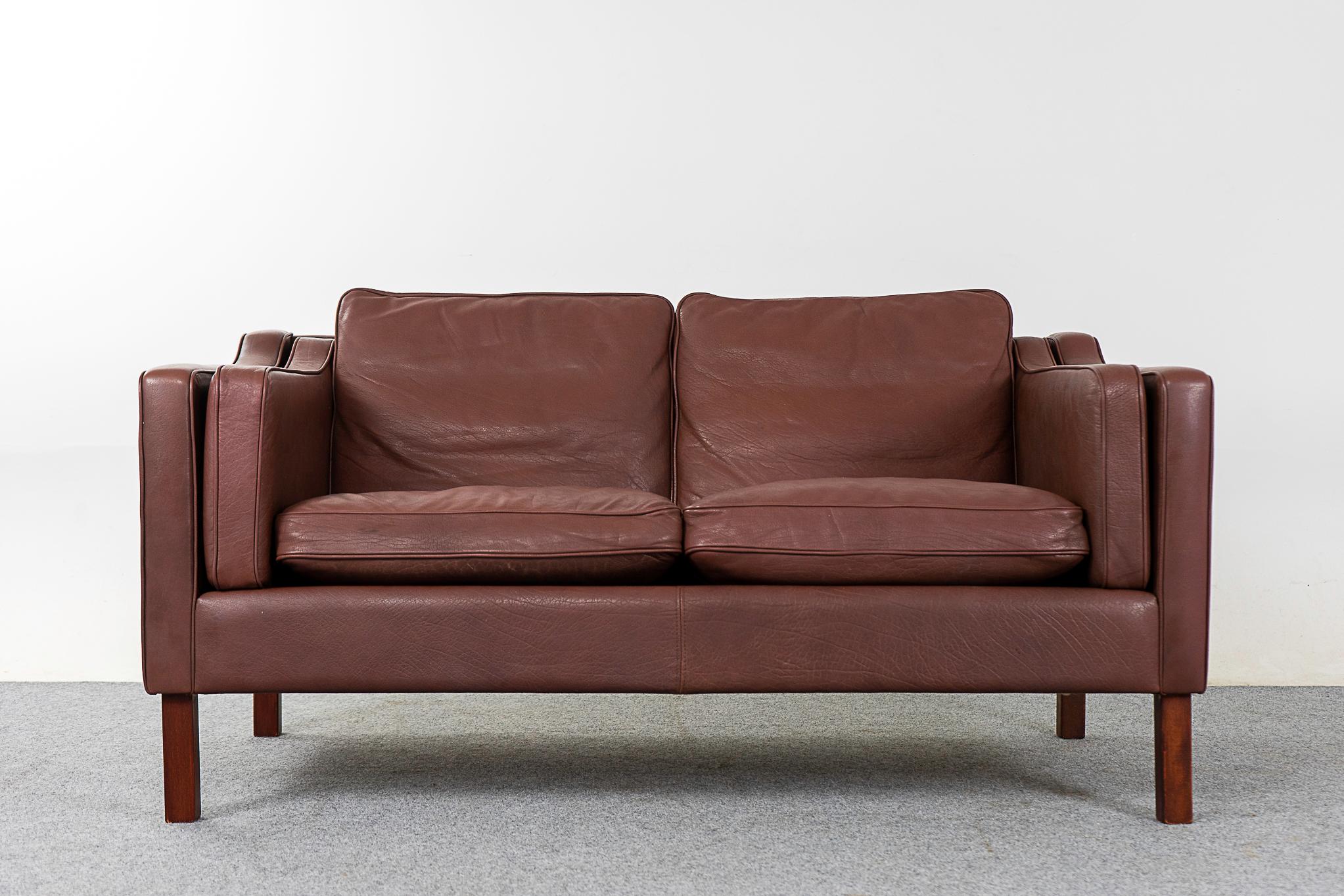 Leather mid-century loveseat, circa 1960's. Cozy, comfortable brown leather, classic modern design. Solid wood legs and compact footprint, some minor marks consistent with age.