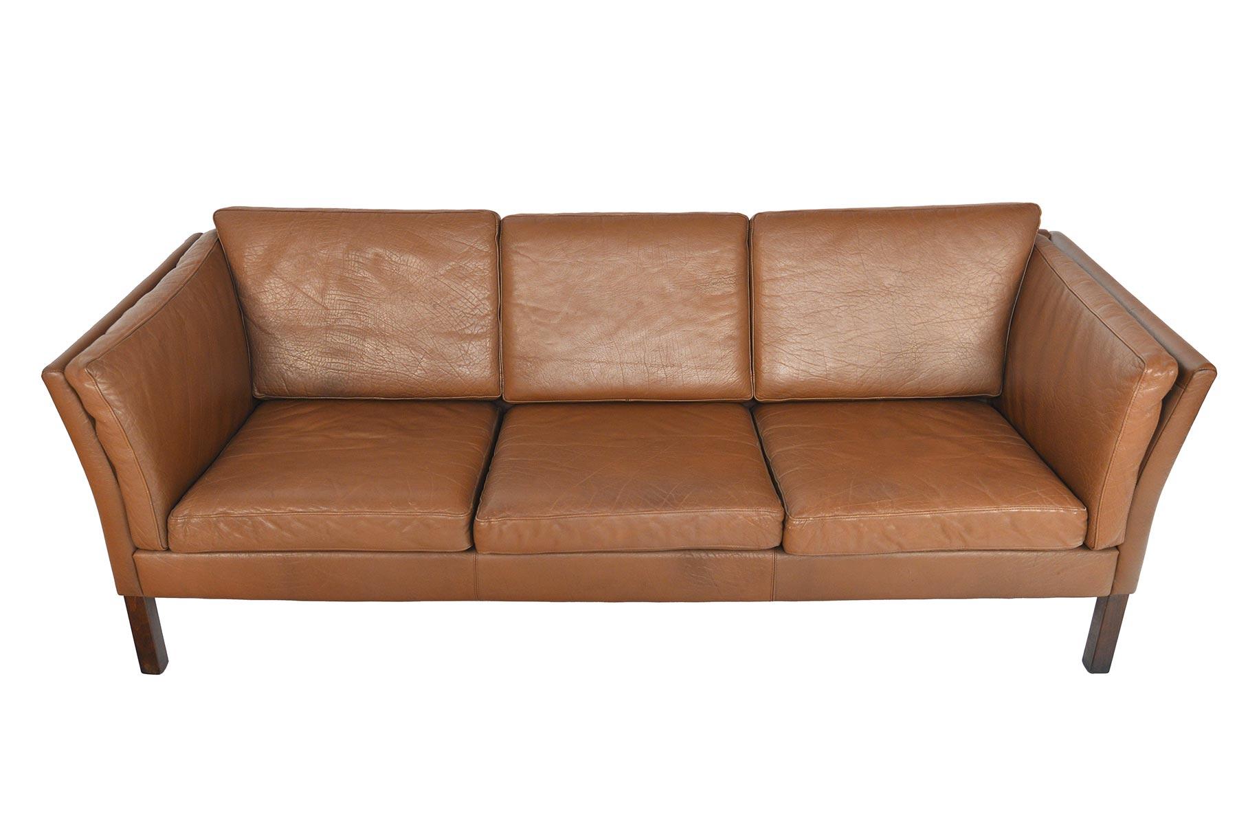This Danish modern sofa is covered in original patinated brown leather. The simple bowed arm design offers an elegant profile. Eight cushions line the interior for a comfortable sitting experience. The sofa stands on a tapered stained beech base.