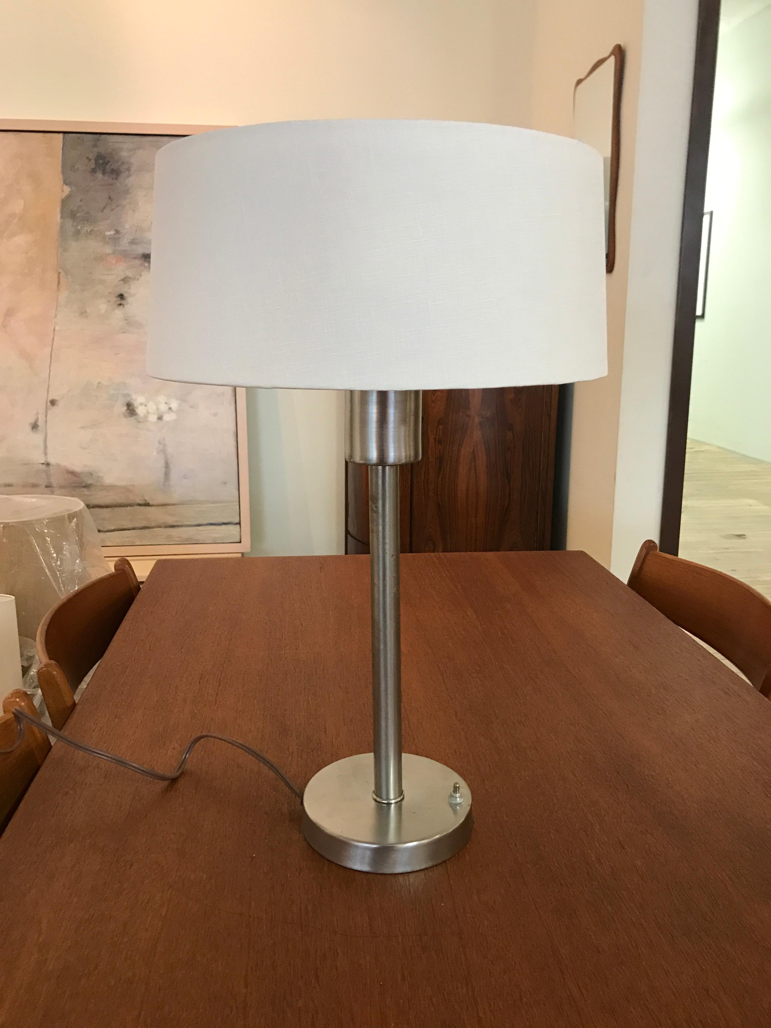 This mid sized brushed stainless steel table lamp with new white linen shade will add simple modern elegance to any room.  Produced by Nessen Studios. 