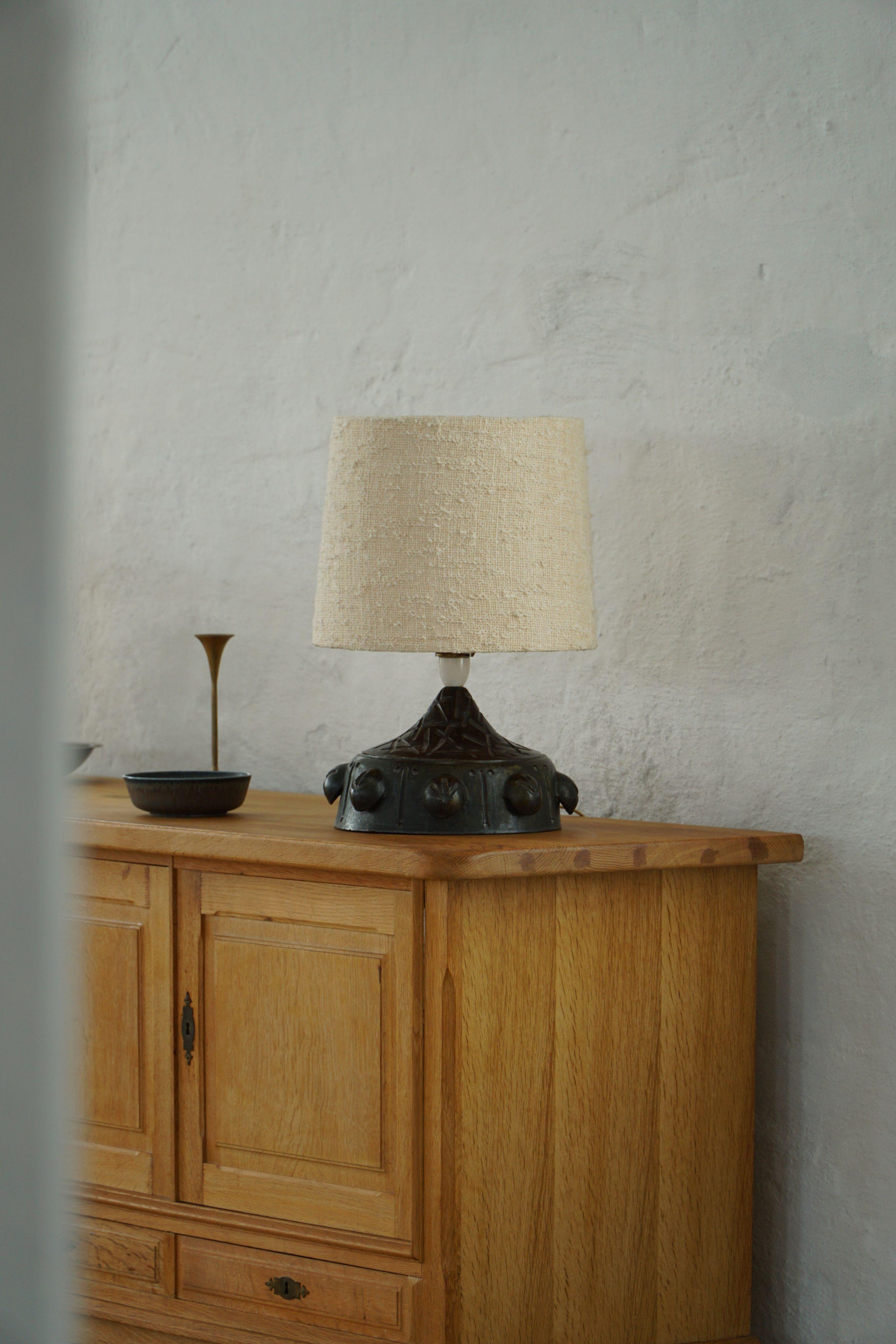 This sculptural table lamp is made of ceramic and has a bold, heavy look that feels both artistic and timeless. The shape is cone-like, with rounded, organic forms placed around the base – almost like buds or seeds ready to bloom. The surface is