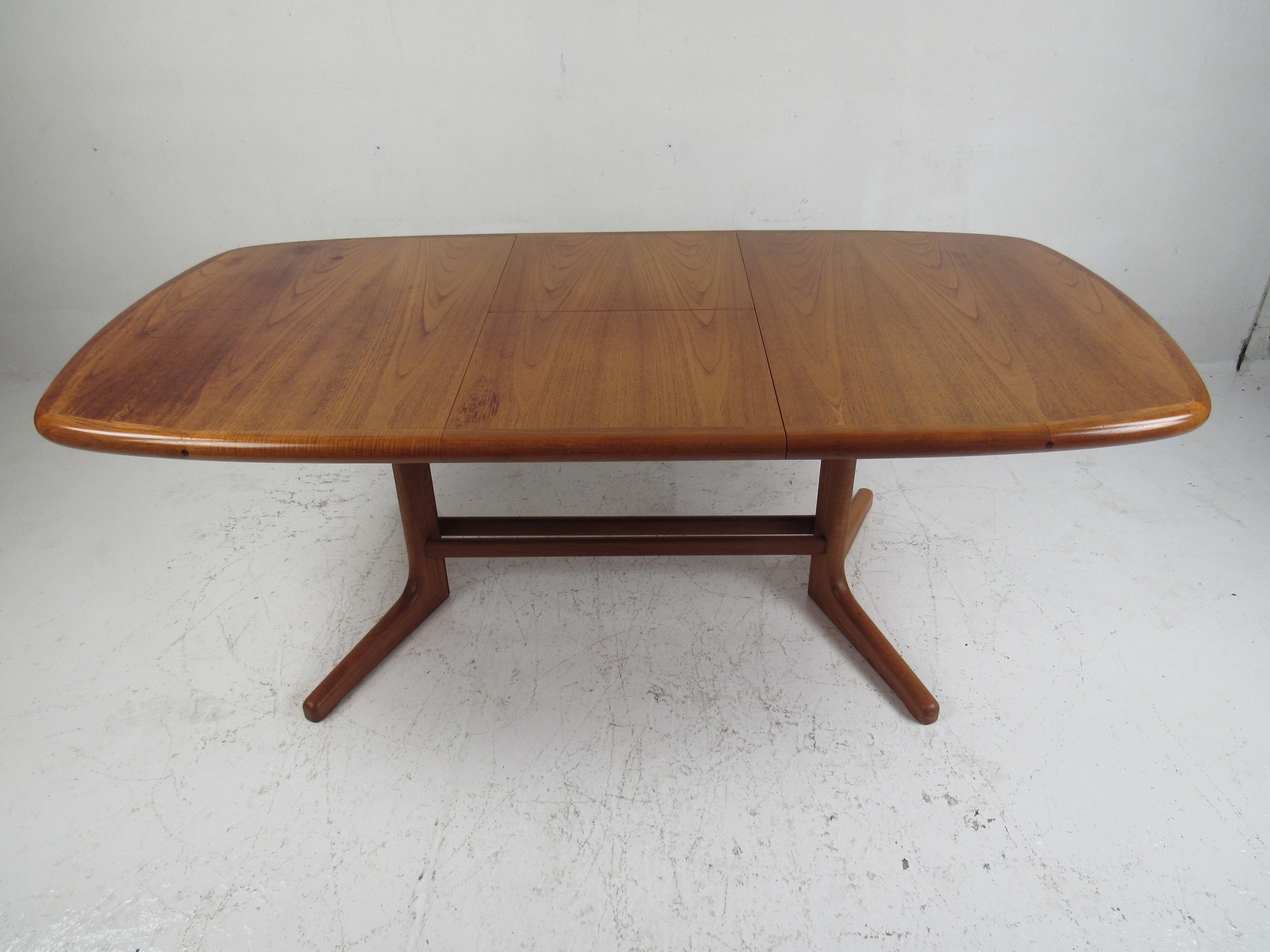 This stunning midcentury teak dining table boasts an unusual butterfly leaf in the middle. This convenient table stores or hides a leaf underneath the center. A unique design that pulls apart unveiling a single leaf in the middle. This lovely piece