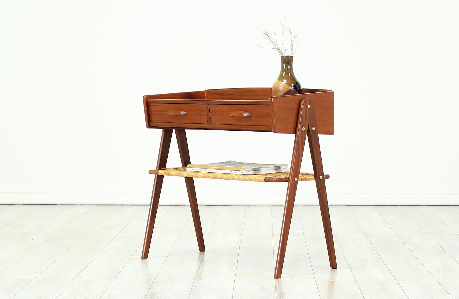 Elegant night-stand designed and manufactured in Denmark circa 1950s. This versatile design features two drawers with carved pulls that provide hidden storage space and a lower caned shelf with its original wicker that serves to hold easily