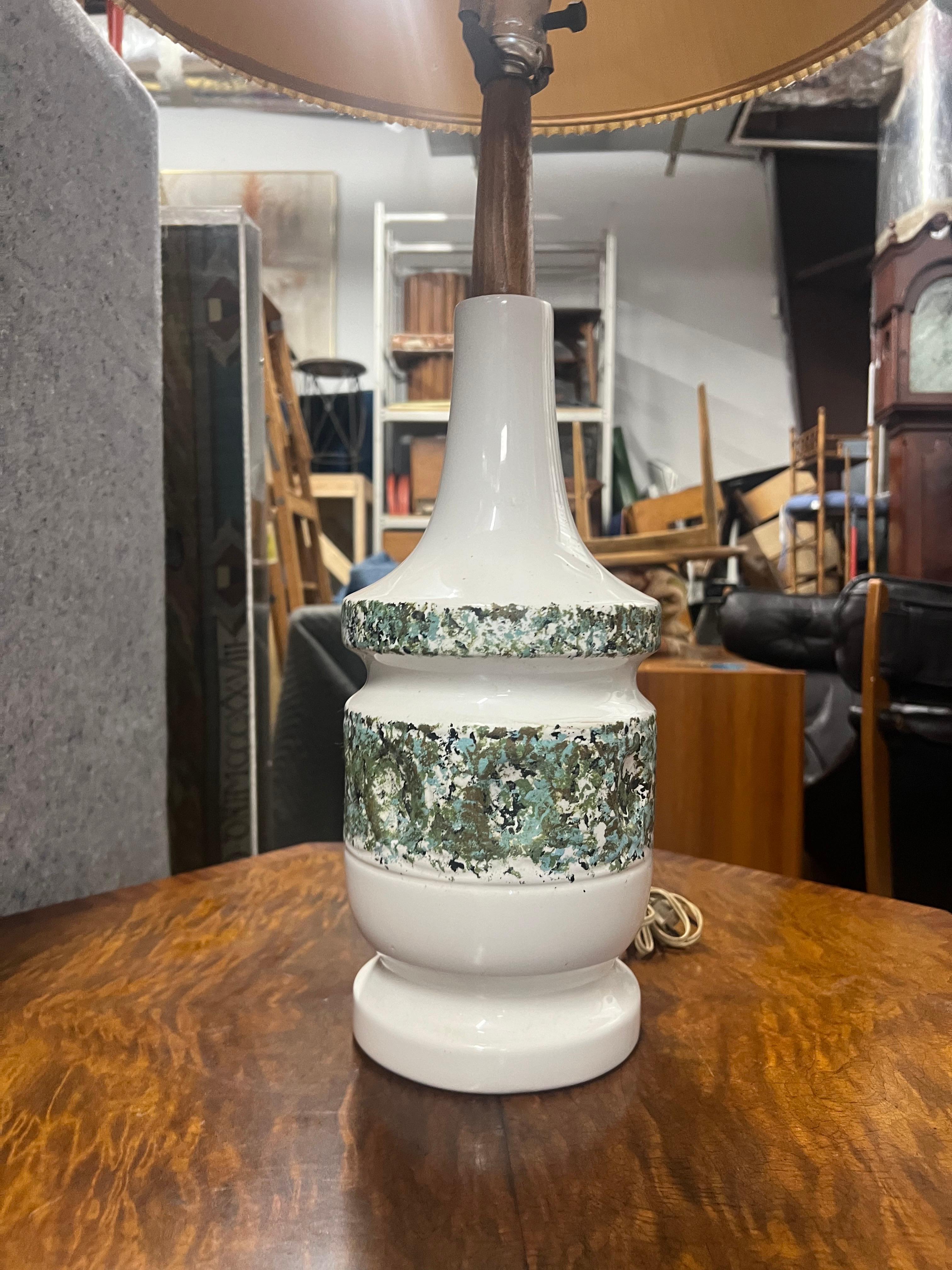 Lampe en céramique émaillée de couleur blanche avec des bleus et des verts comme couleurs d'accent.  Un beau manche en teck.   Cette lampe a une forme superbe et n'est pas si imposante avec l'abat-jour plissé.  
L'abat-jour mesure 7