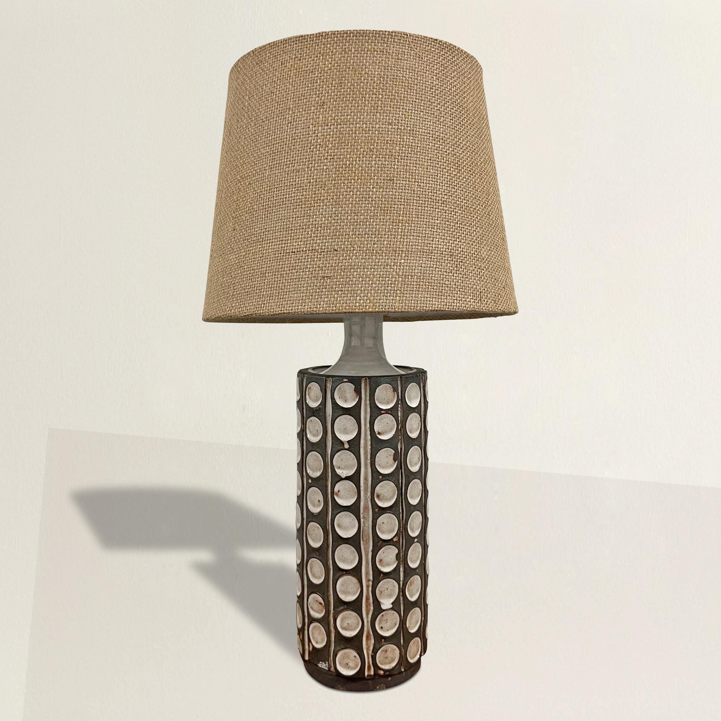 Illuminate your space with the understated elegance of mid-20th century Danish modern design embodied in this ceramic table lamp. Its cylindrical form showcases the unglazed clay against a striking white glaze pattern of repeated stamped circles and
