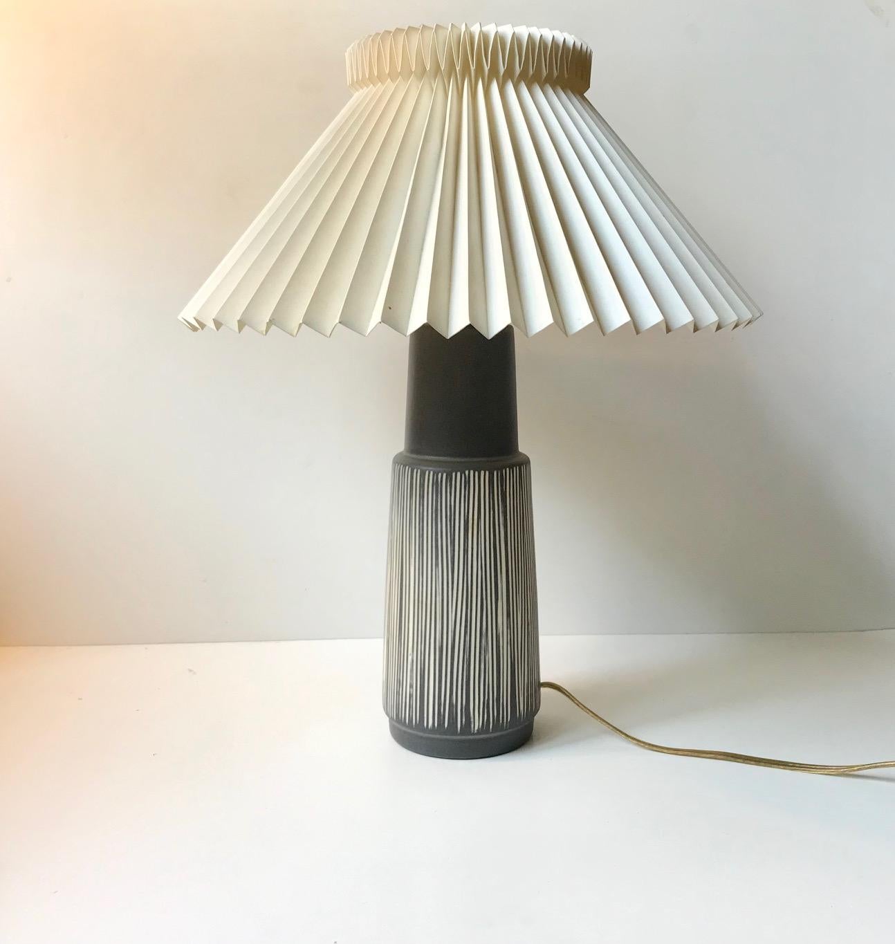 - Ceramic table lamp decorated with white vertical stripes on a satin grey main glaze
- Designed and manufactured by Elisabeth Loholt in Denmark during the 1950s in a style reminiscent of Palshus, Rorstrand and Ingrid Atterberg in particular.
-