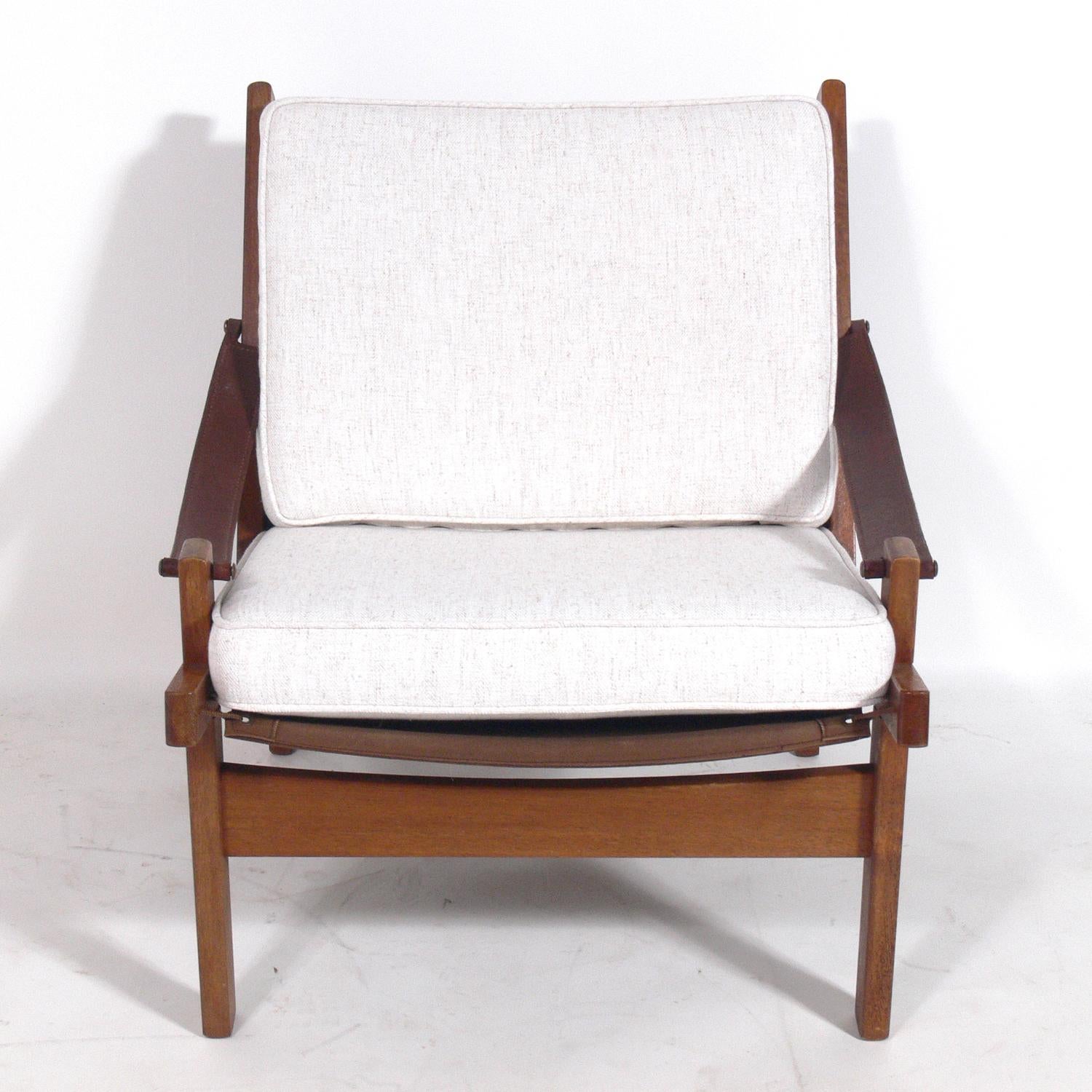 Danish modern chair with leather strap arms, Denmark, circa 1960s. It has been reupholstered in an ivory color herringbone fabric. The wood and leather retain their warm original patina.