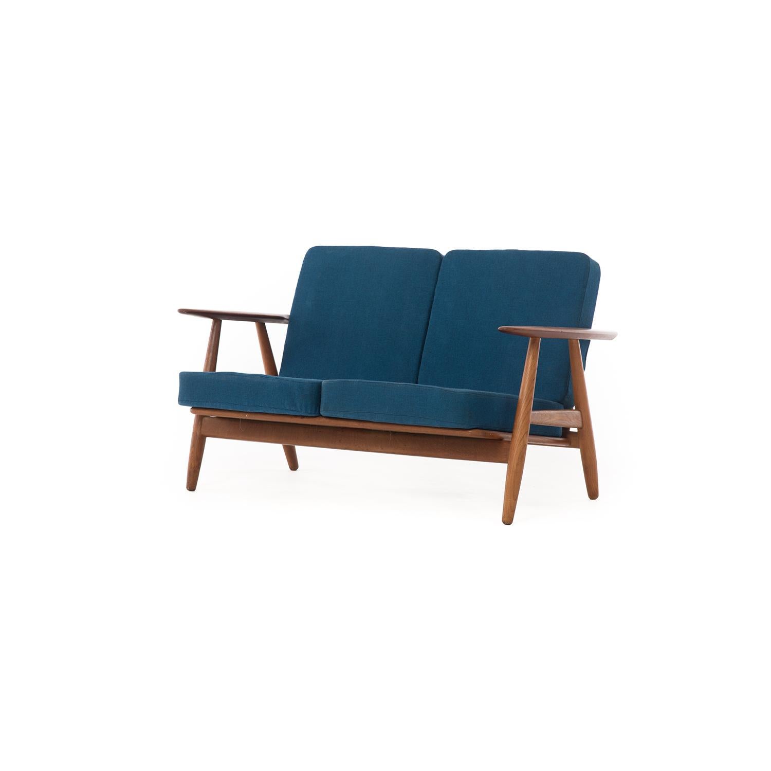 Easily recognizable as a midcentury settee, this Danish modern cigar settee is a little piece of the past that adds a subtle statement to any room. The frame is solid, made of teak and oak. The cushions, in a saturated blue, show minor wear— it's a