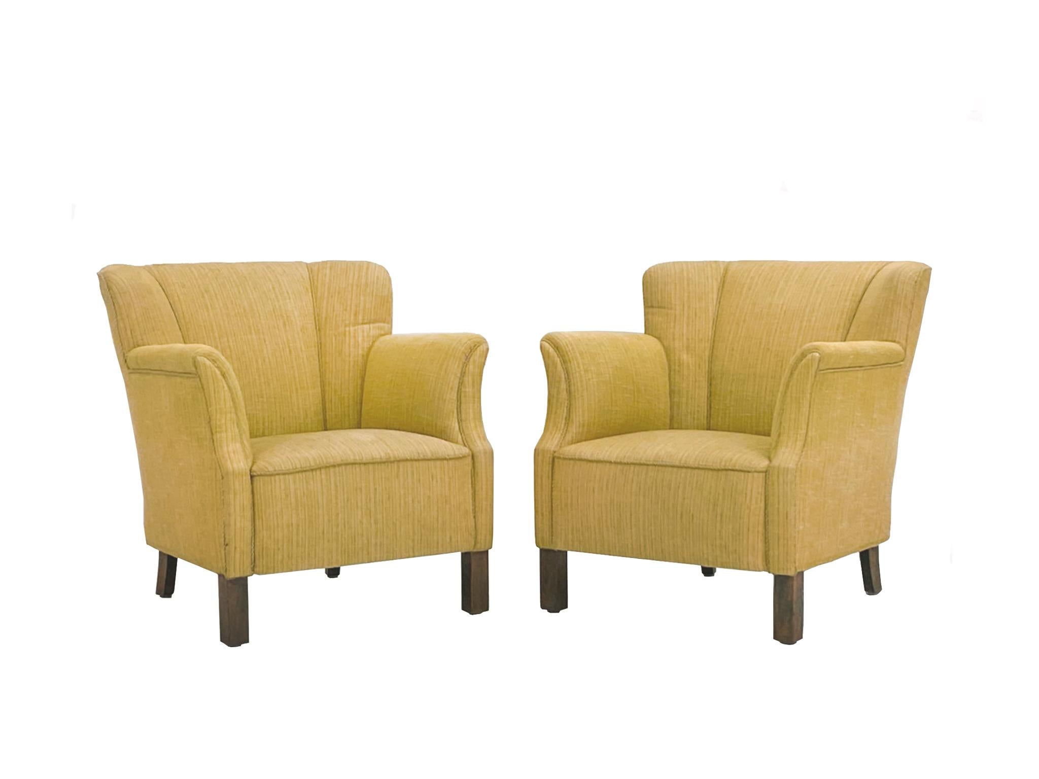 Crafted in the 1950s, these Danish Modern club chairs were designed in the style of Frits Henningsen. They have oak legs and yellow linen upholstery. Rounded, full forms - enhanced by the channeled back and rope piping - characterize the silhouette