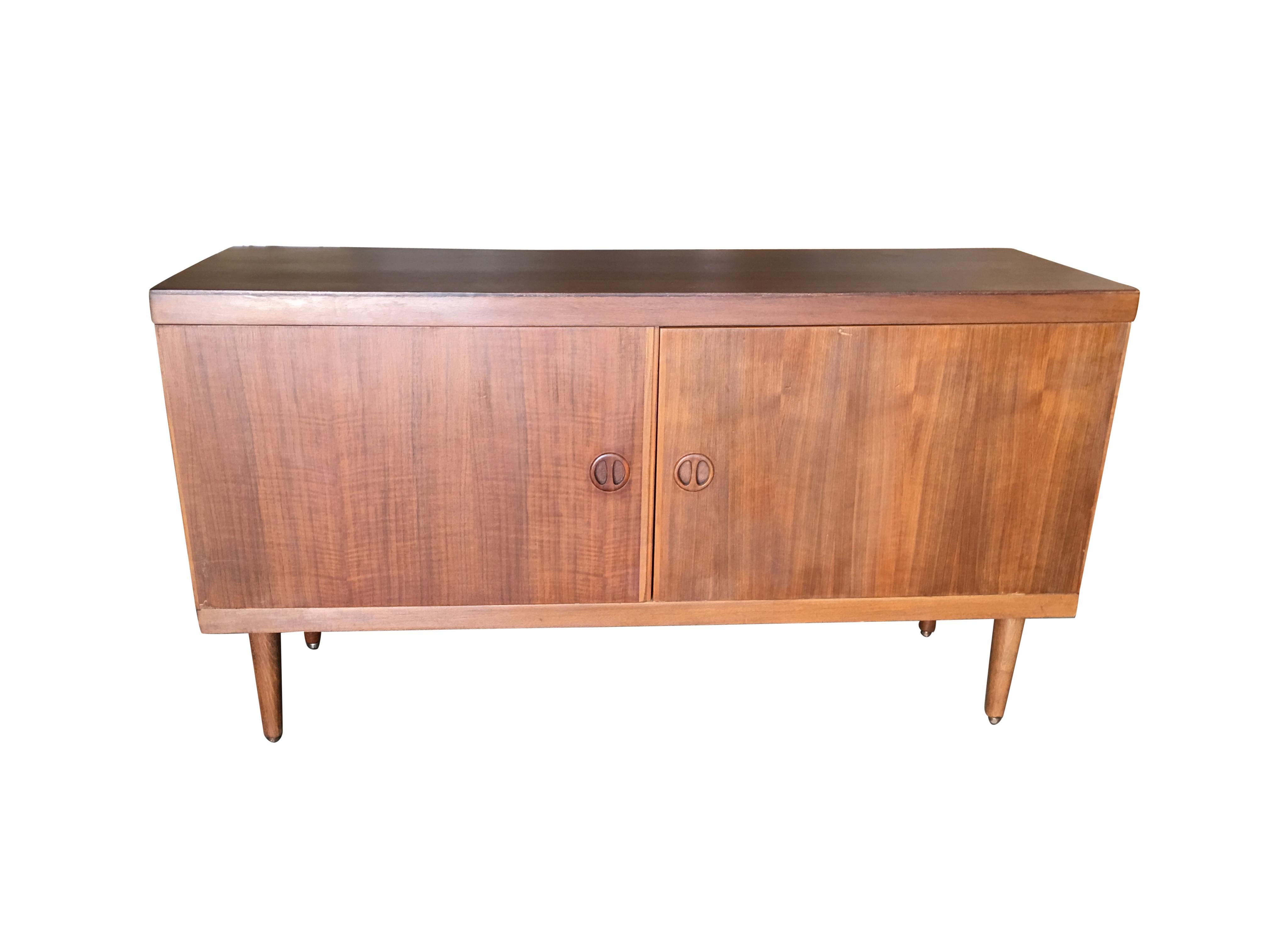 This small Danish style rose stained credenza cabinet with tapered legs, sculpted pig nose pulls, fancy hinges and two easy swing doors. It features two large chubby spaces for storage. 

The cabinet is a great size for a smaller dwelling or for