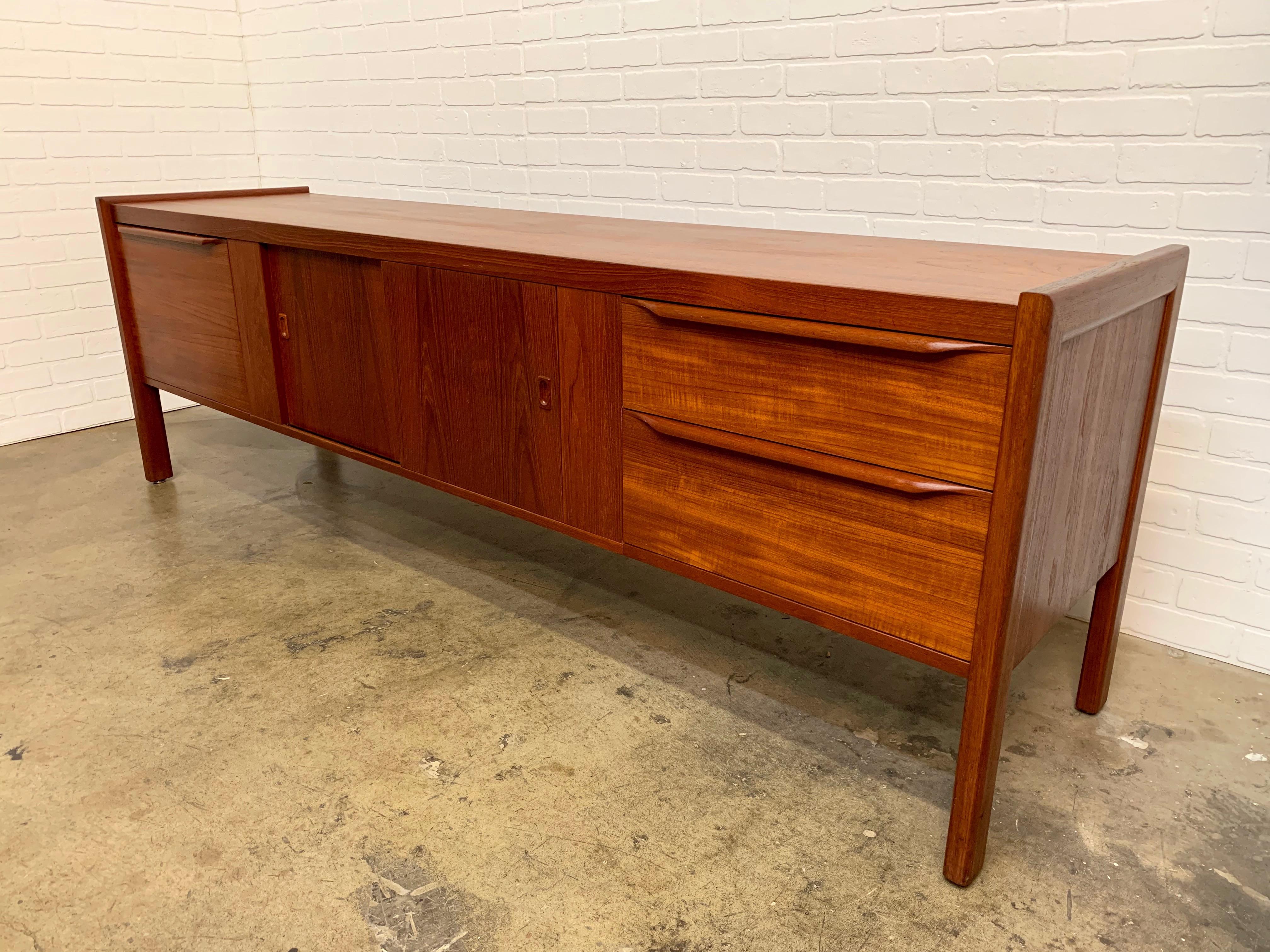 Long and low teak Danish modern credenza with sculpted drawer pulls and sliding door storage in the center.
